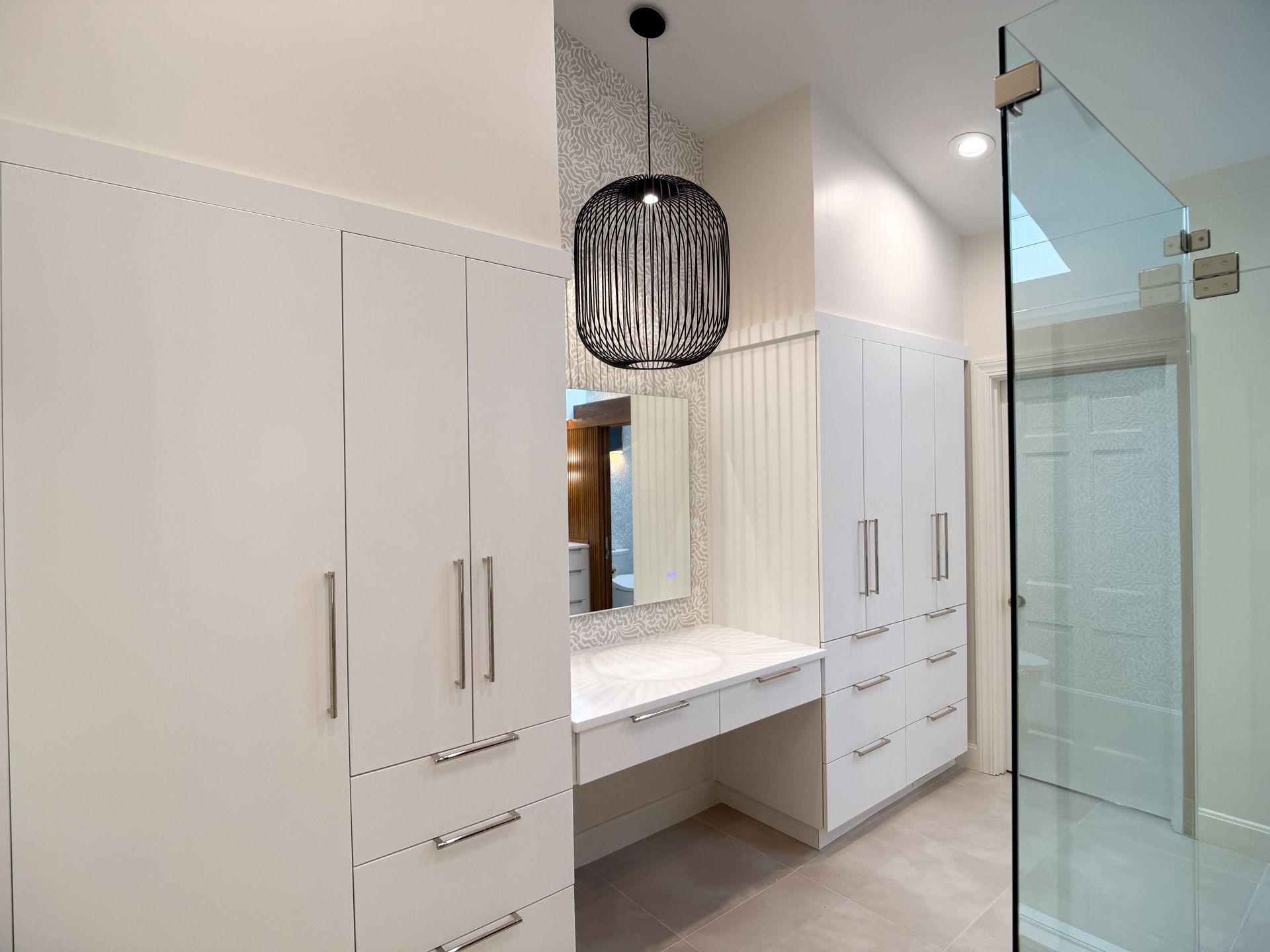 Modern bathroom with white cabinets, vanity, mirror, pendant light, and glass shower enclosure