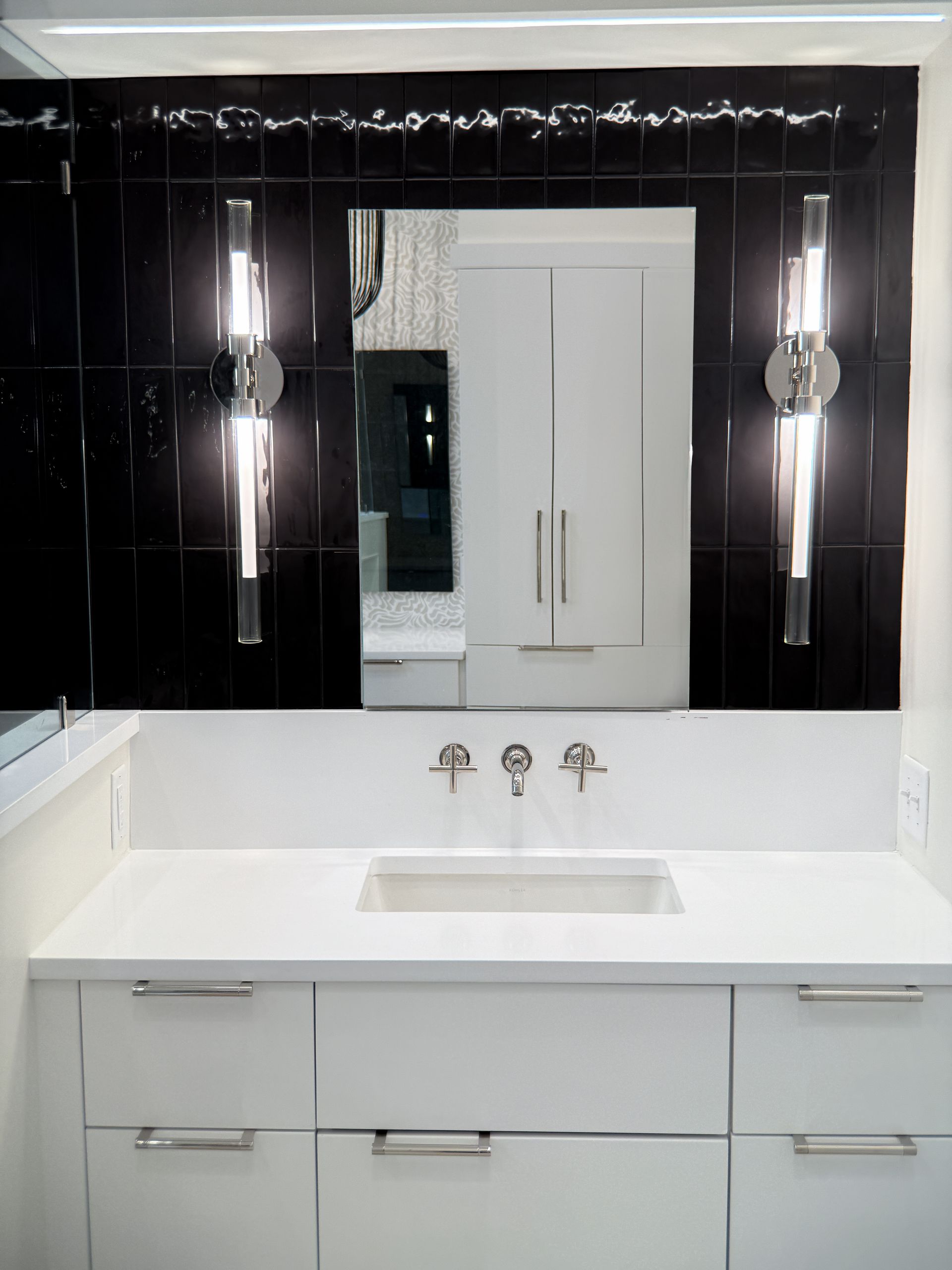 Modern bathroom vanity with white sink, mirrored cabinet, and wall sconces against a black accent wall