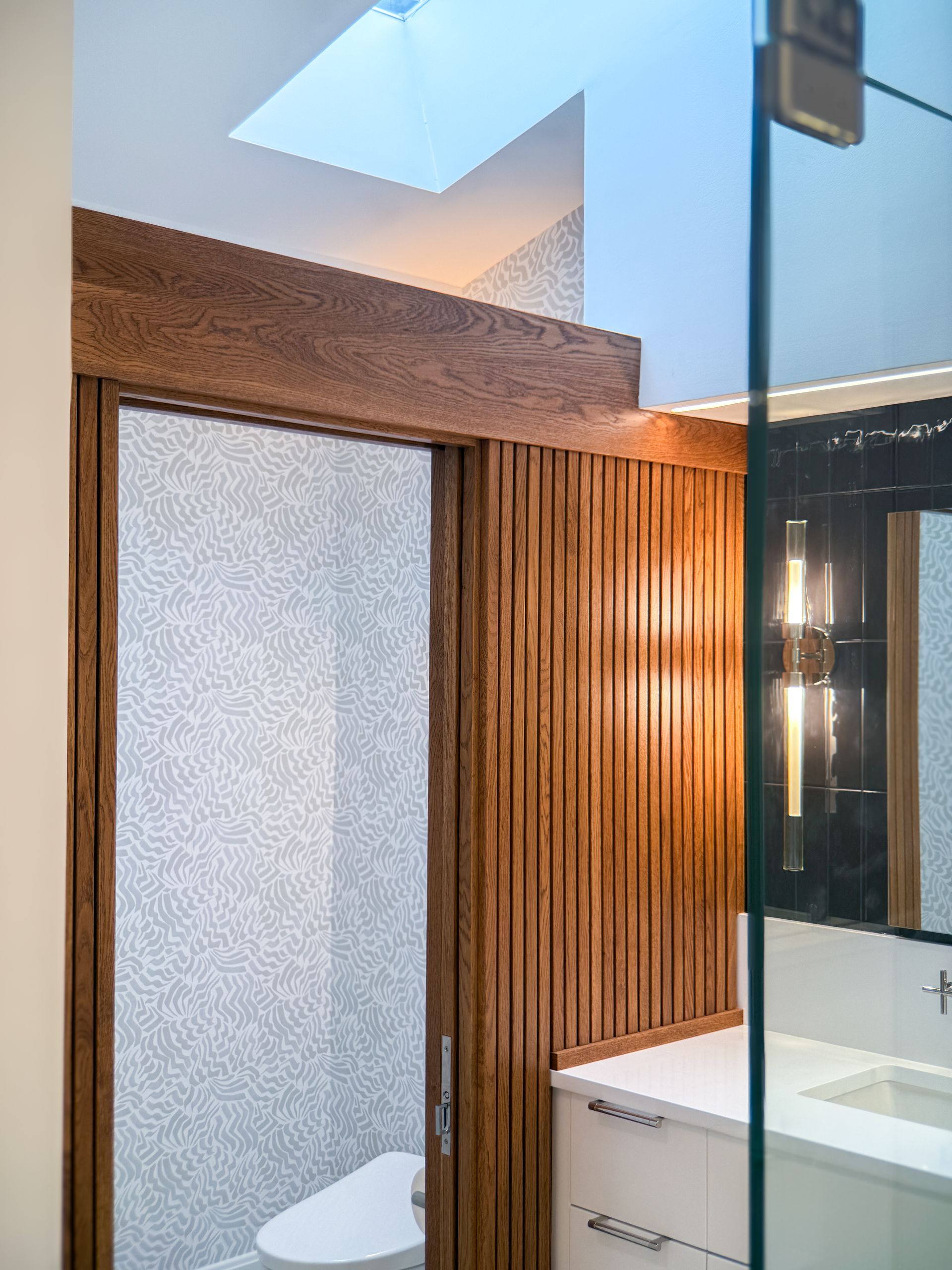 Modern bathroom with frosted shower door, wood accent wall, and a white sink vanity with mirror.