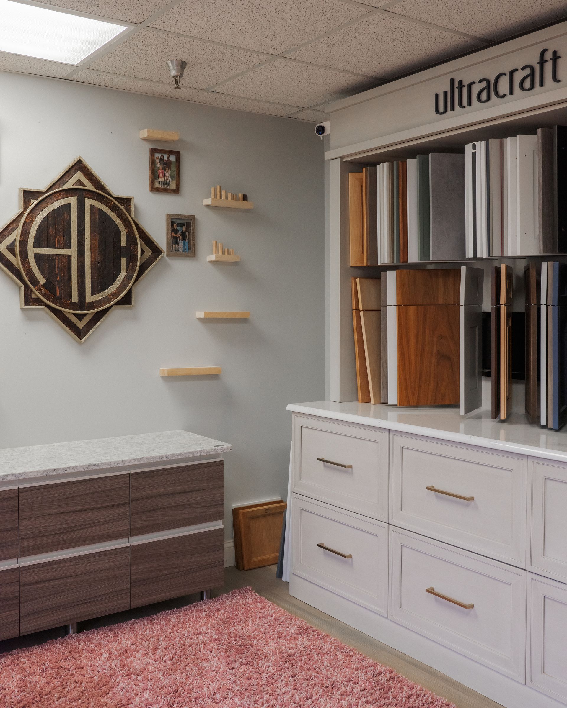 Showroom with display shelves, cabinets, and sample finishes on a light gray wall and pink rug.