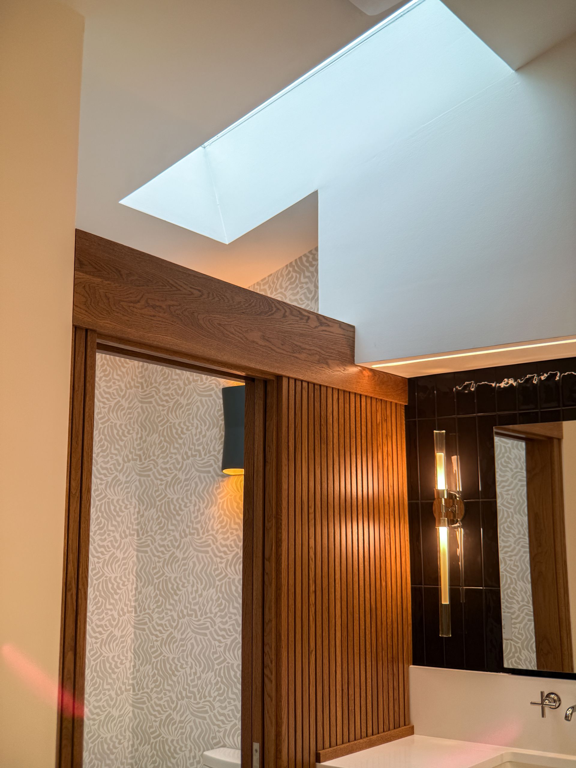 Modern bathroom with skylight, wood paneling, and warm wall lighting