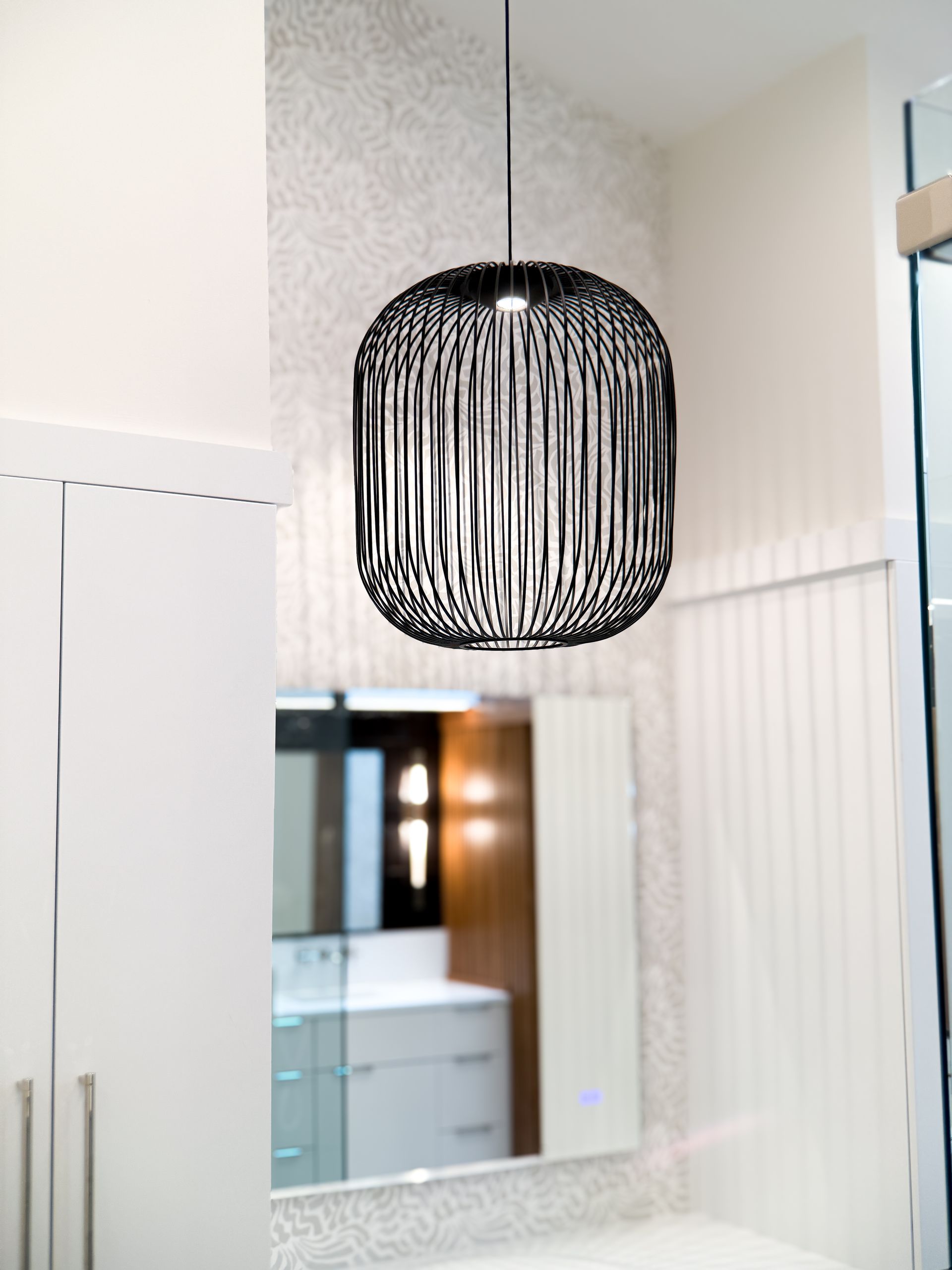 Black woven pendant light hanging in a modern bathroom with a mirror and white walls