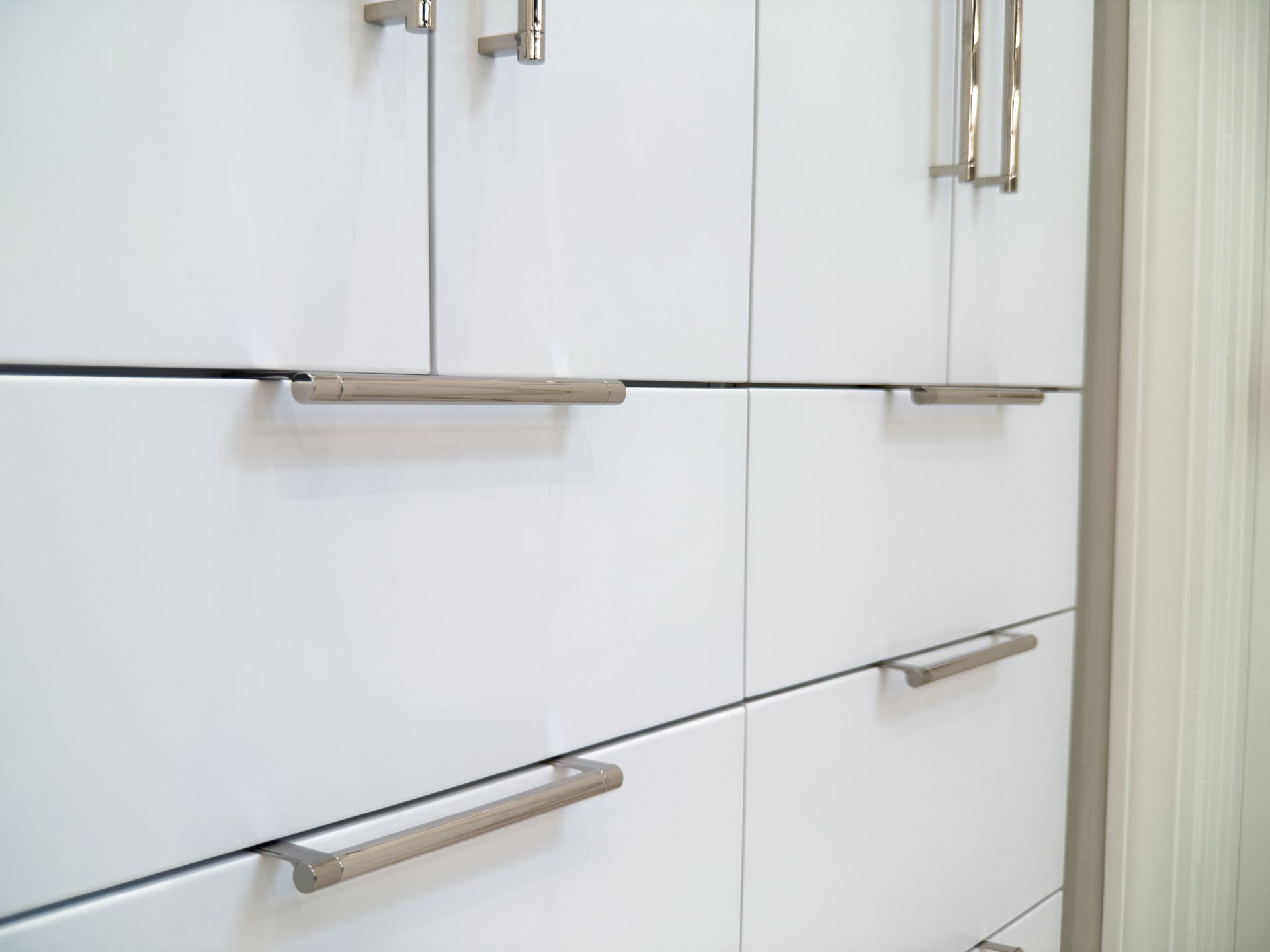 White kitchen cabinets with silver handles and a light wood floor sliver visible below