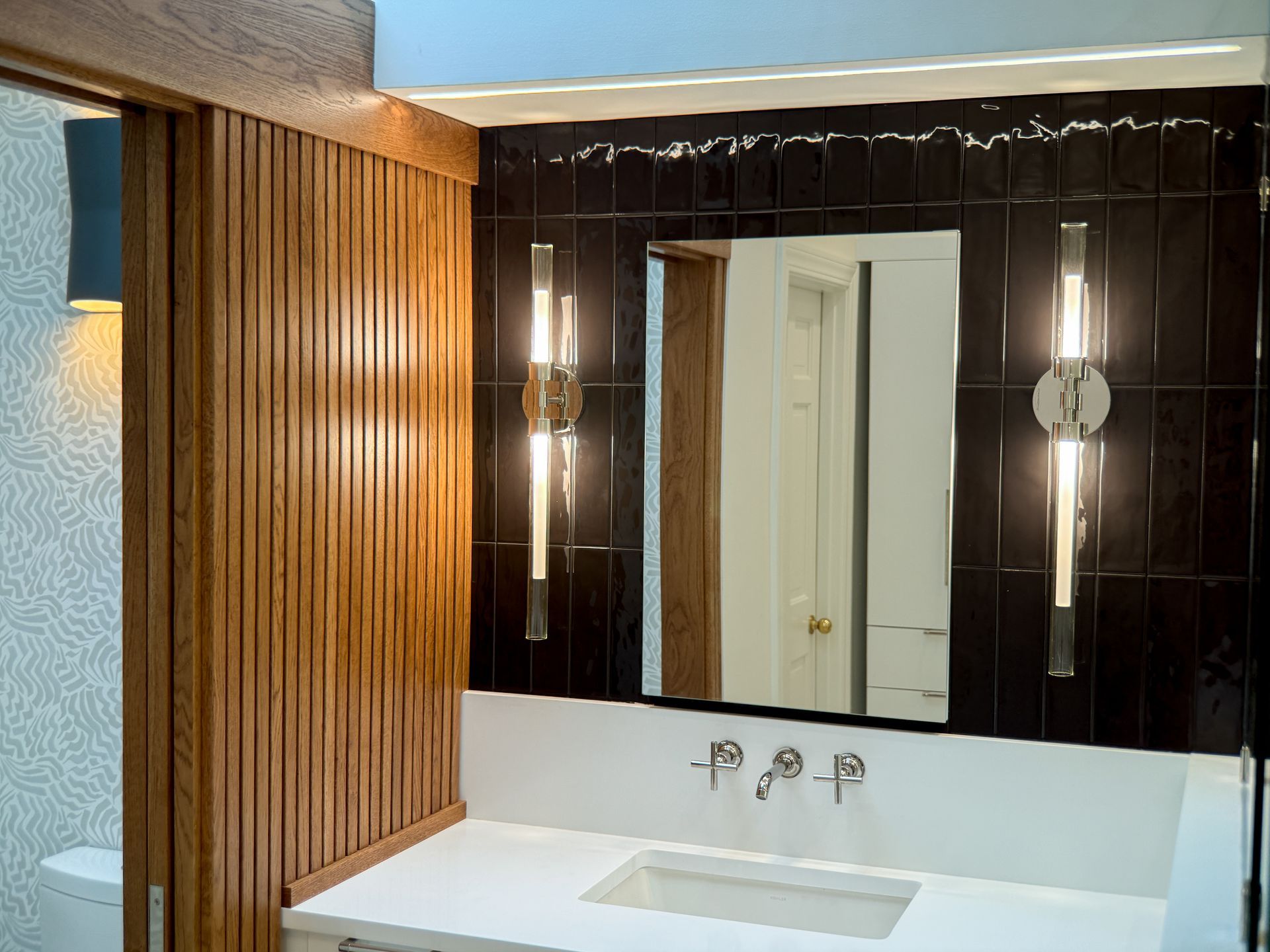 Modern bathroom vanity with mirror, white sink, dark tile, and wood slat accent wall