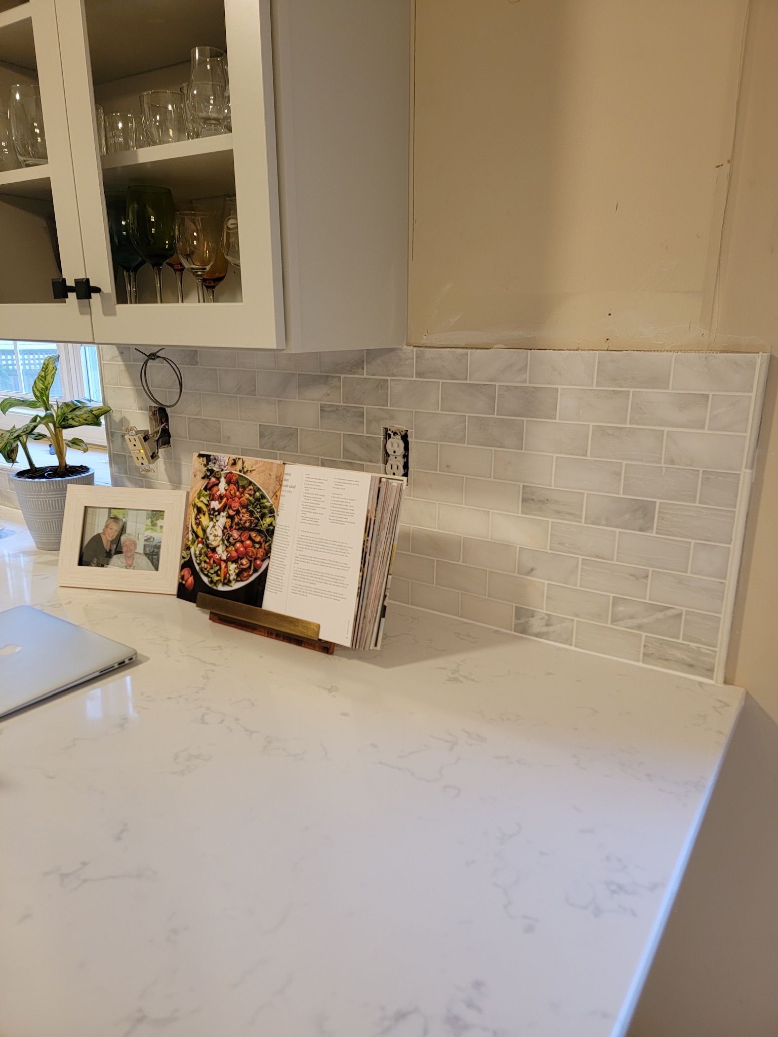 White kitchen counter with backsplash, cabinet, and a few photo cards leaning against the wall.