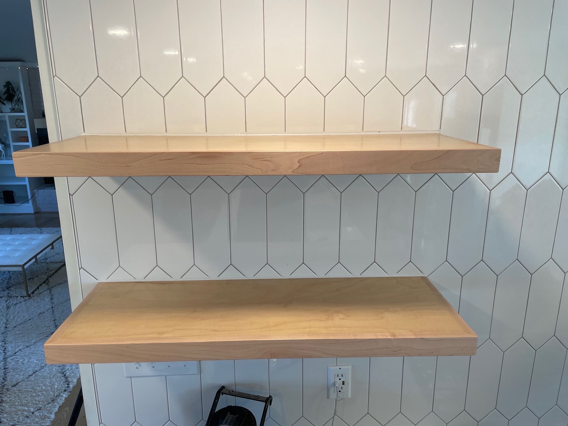Two wooden floating shelves mounted on a white tiled wall in a kitchen.