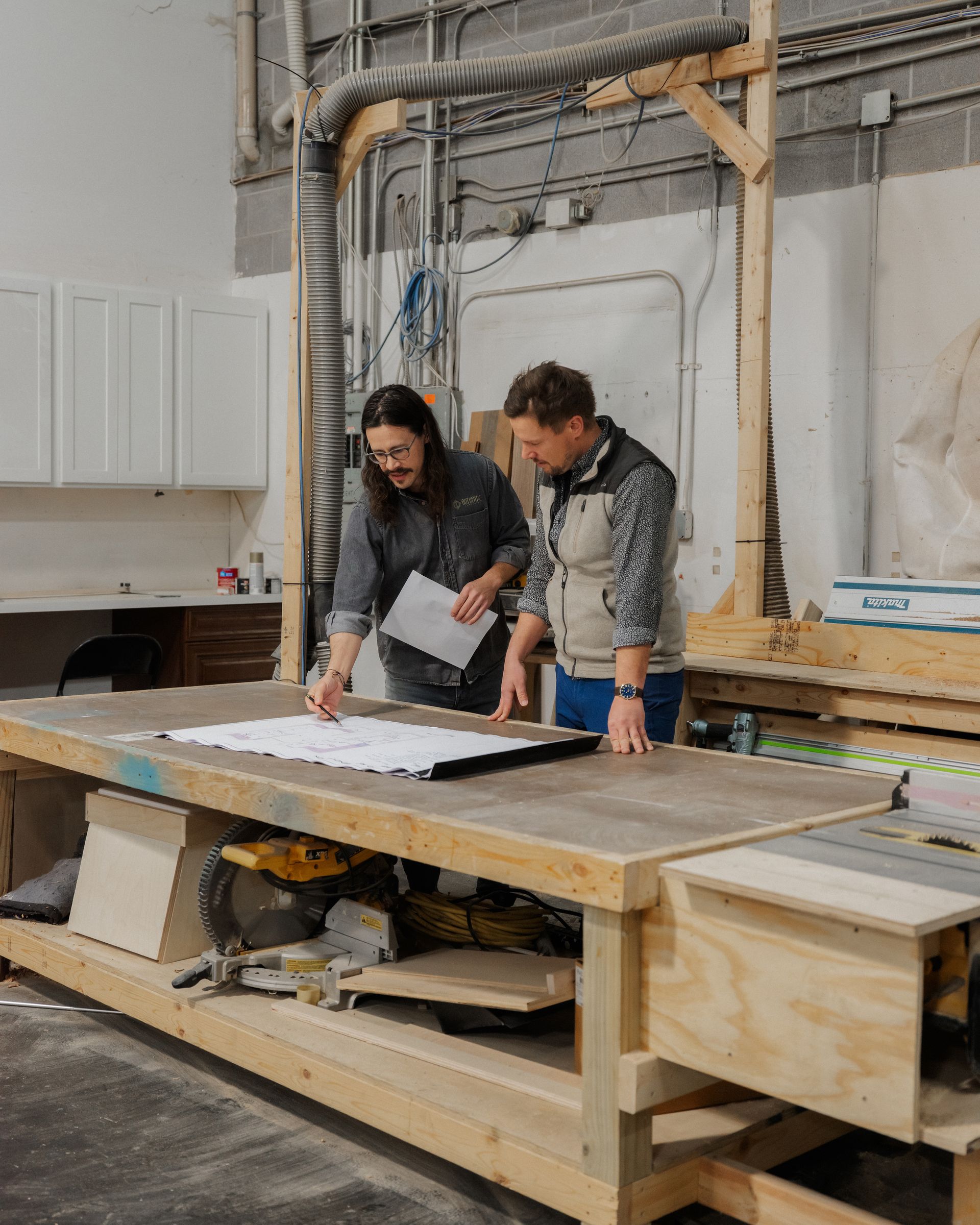 Two people reviewing plans on a large wooden workbench in a workshop
