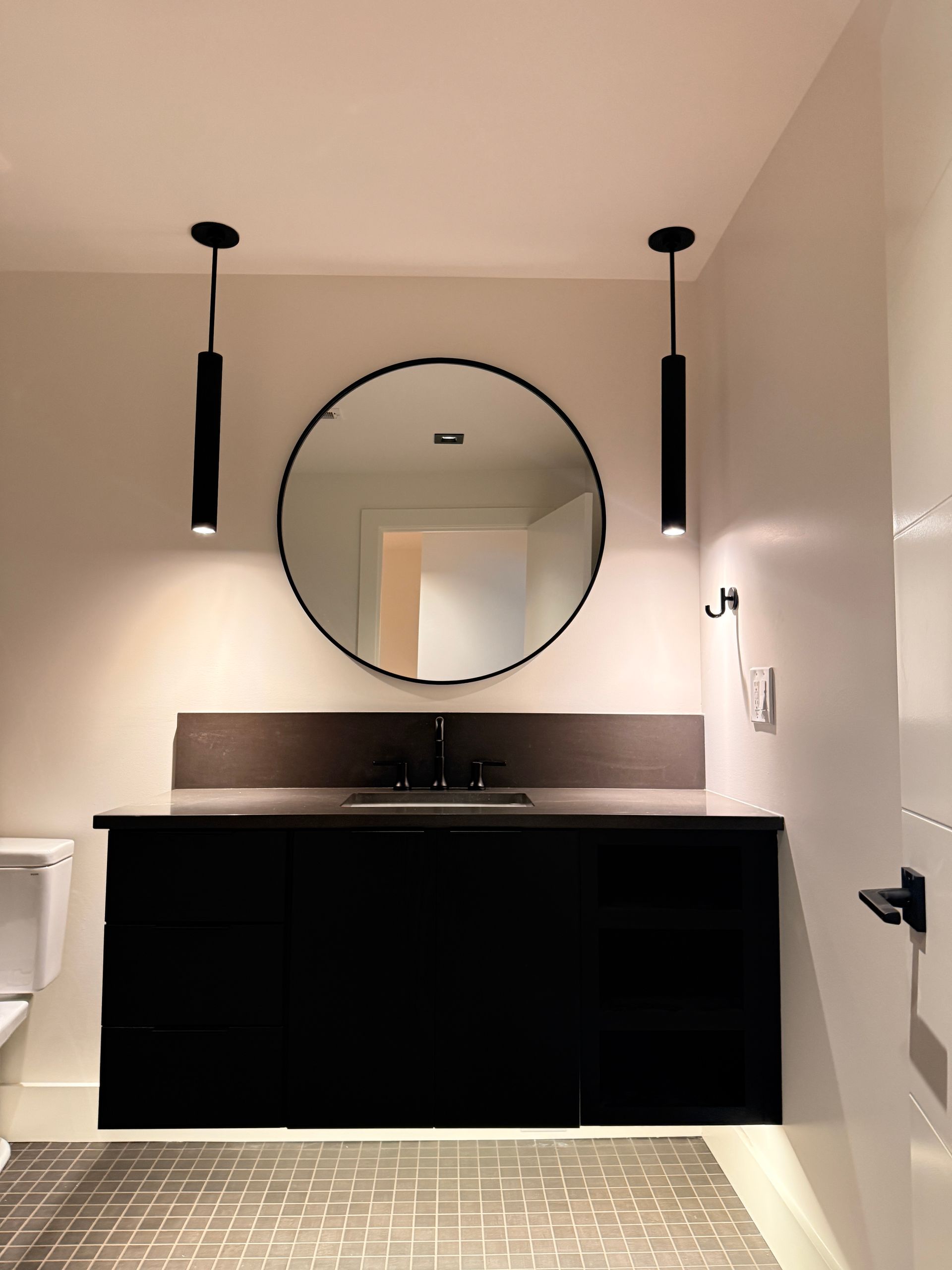 Modern bathroom vanity with round mirror, black cabinet, and two hanging pendant lights.