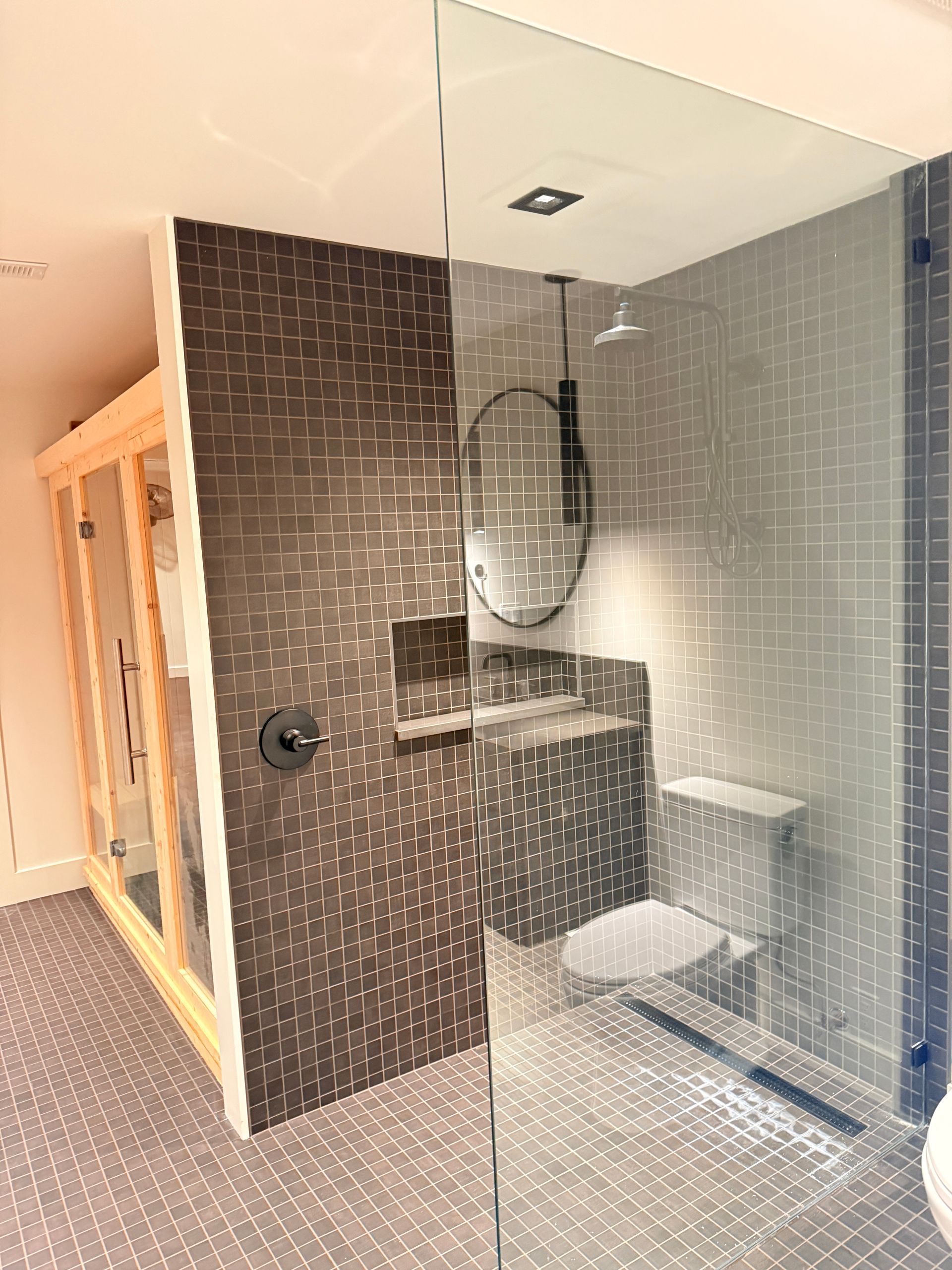Modern bathroom shower with dark tile wall, glass partition, mirror, and built-in bench