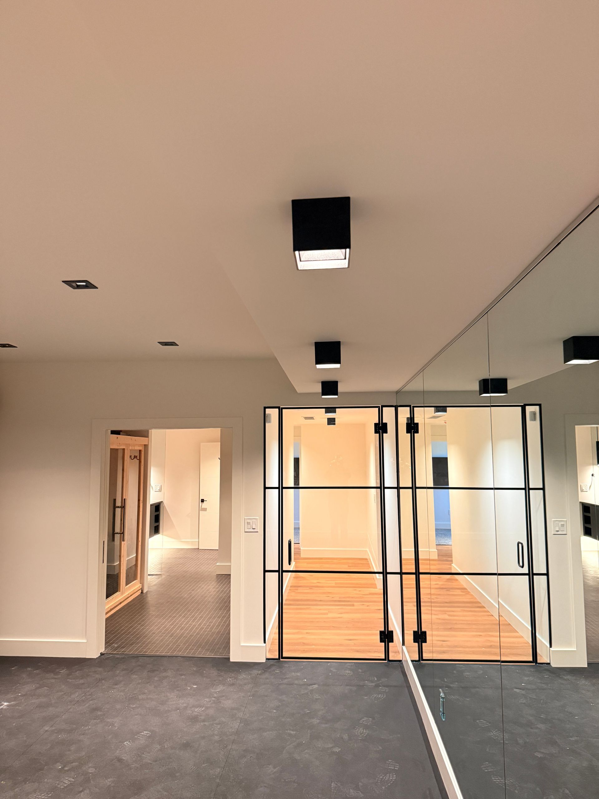Modern office hallway with glass doors, gray carpet, and wood flooring under ceiling lights