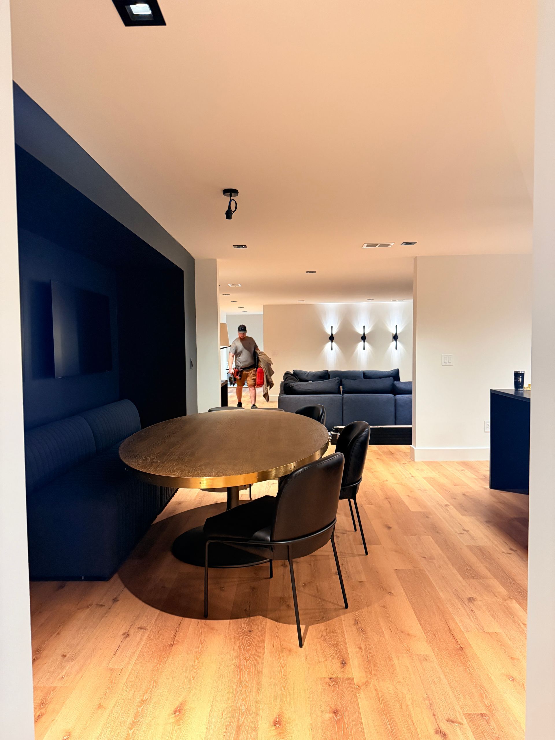 Modern dining area with dark blue walls, round wooden table, black chairs, and a blue sofa in the background