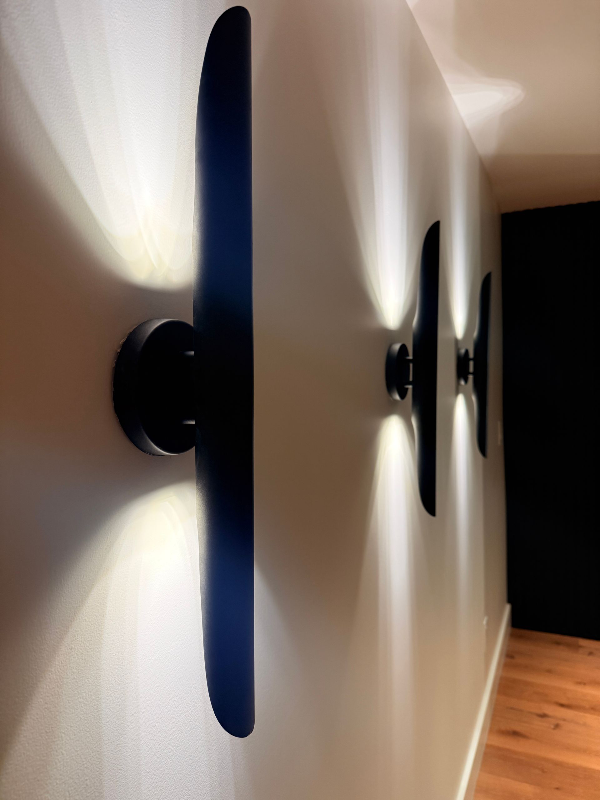 Wall sconces casting soft light along a white hallway with wood flooring
