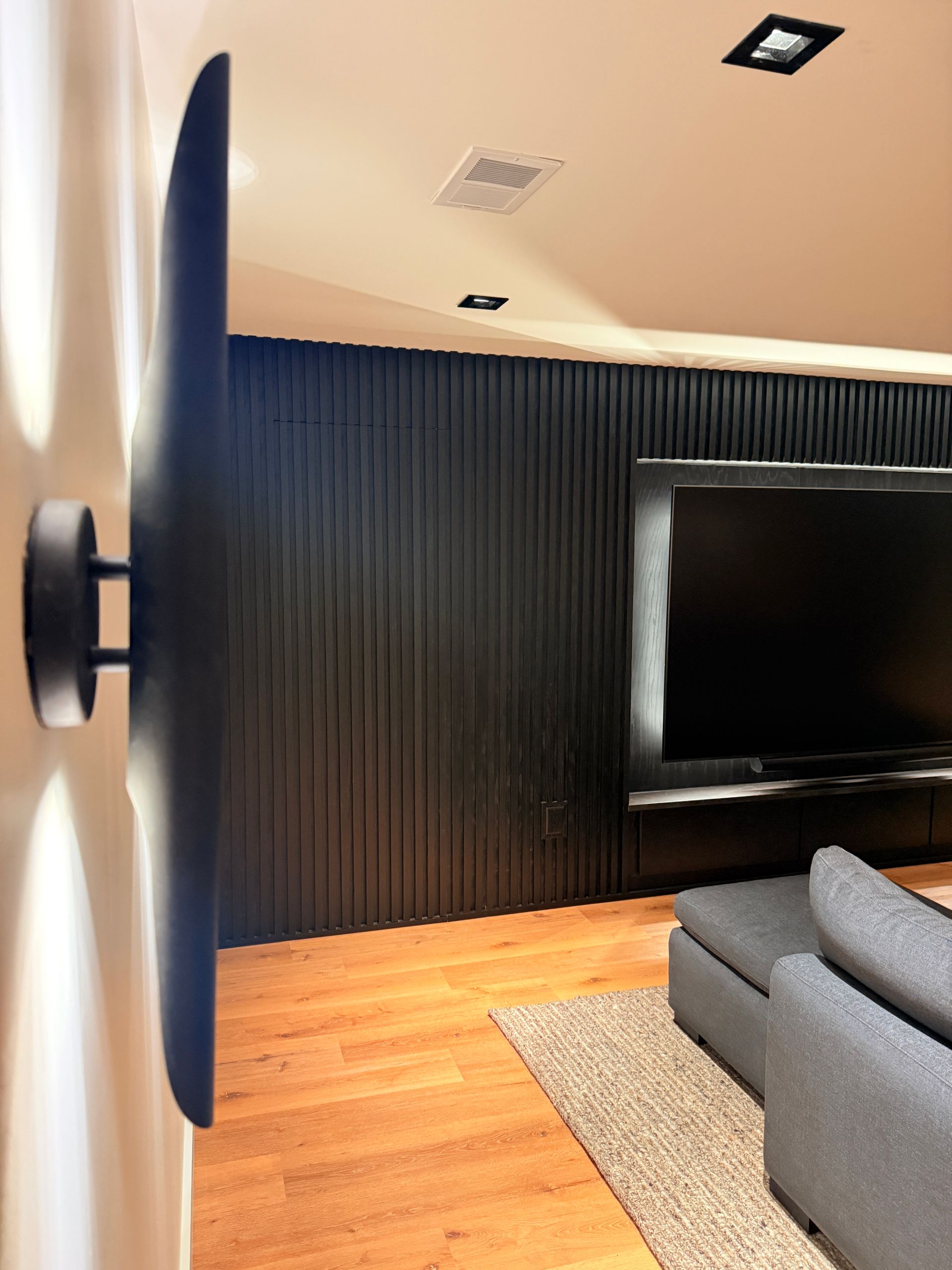 Modern living room with black accent wall, wall-mounted TV, gray sofa, and warm wood floor