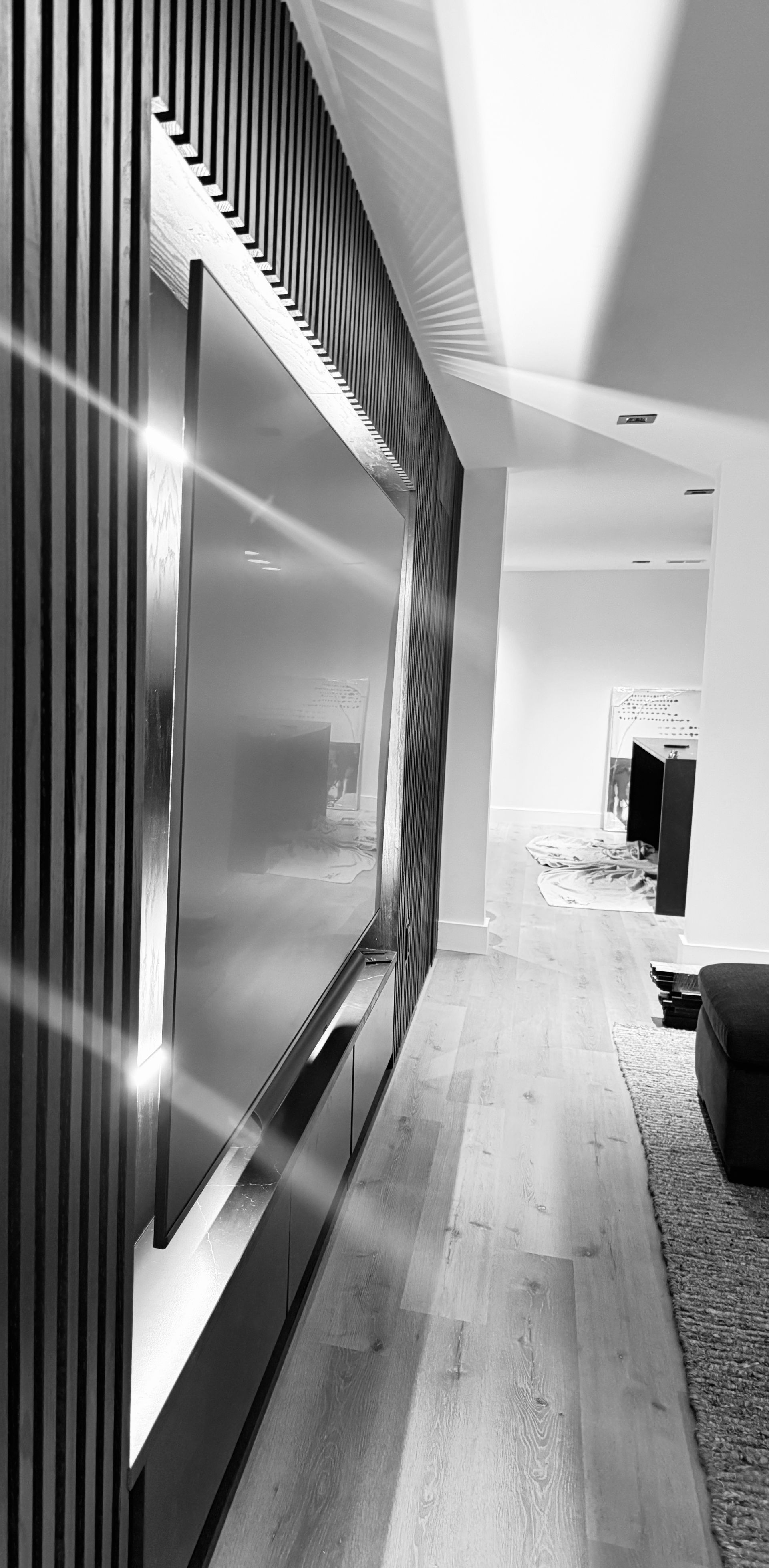 Black-and-white modern hallway with a large wall-mounted TV and bright windows in the distance