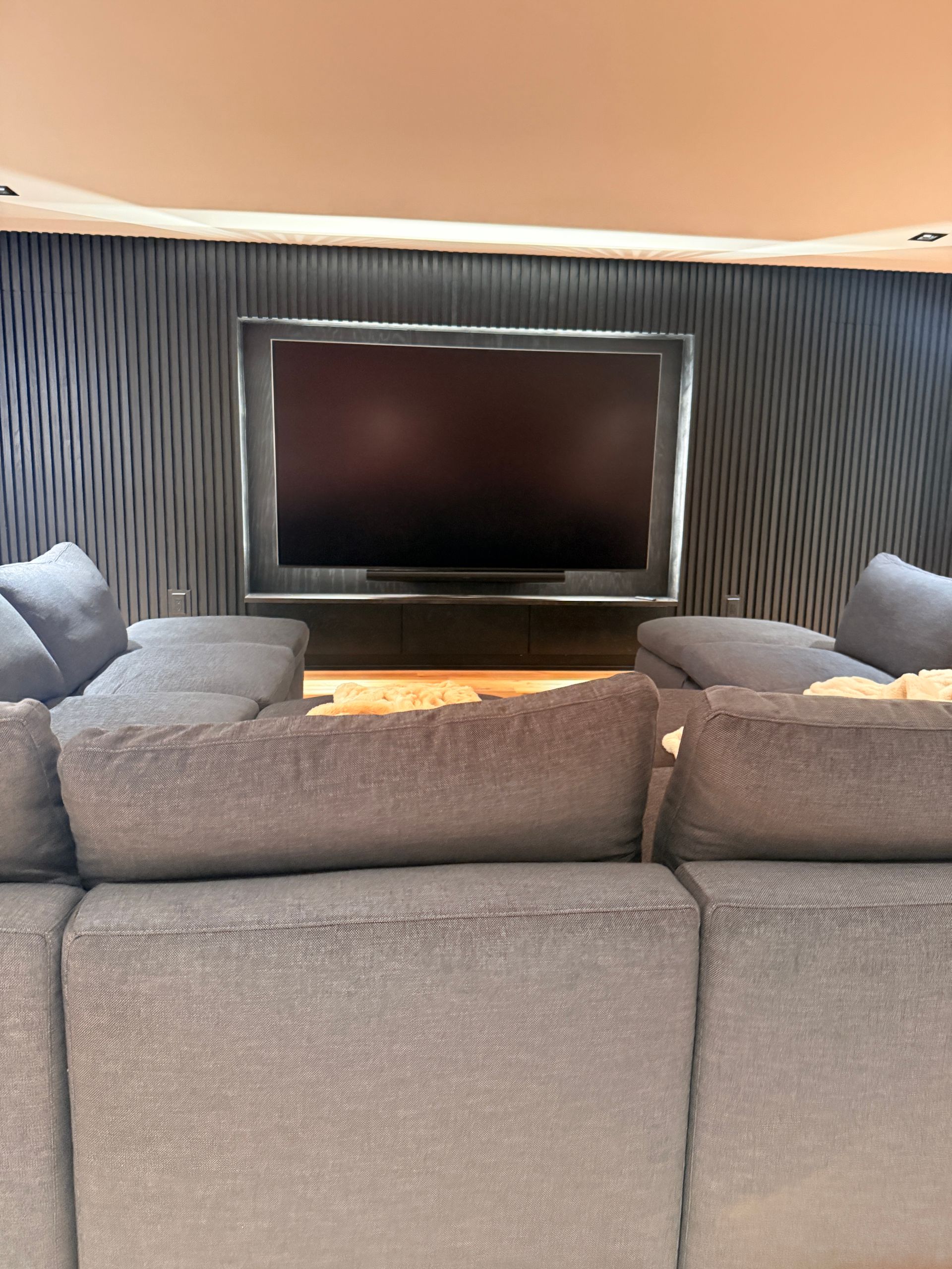 Modern lounge with gray sectional sofas facing a wall-mounted TV and striped accent wall