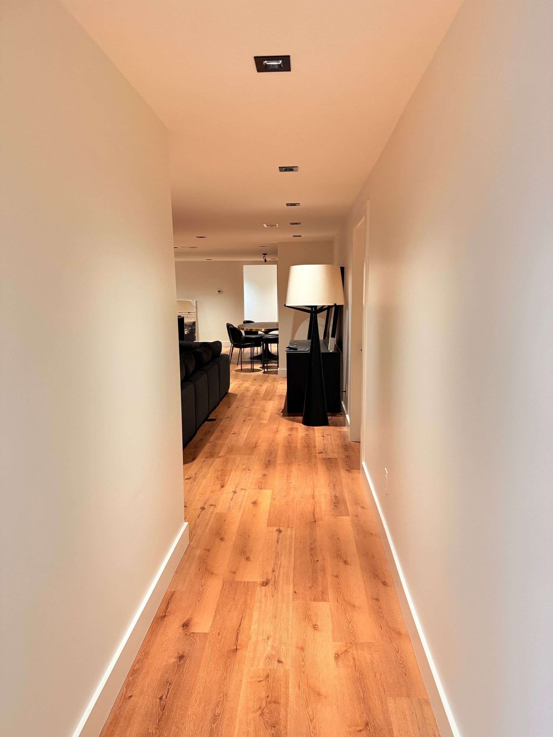 Long narrow hallway with wood floors leading to a living room with a sofa and lamp