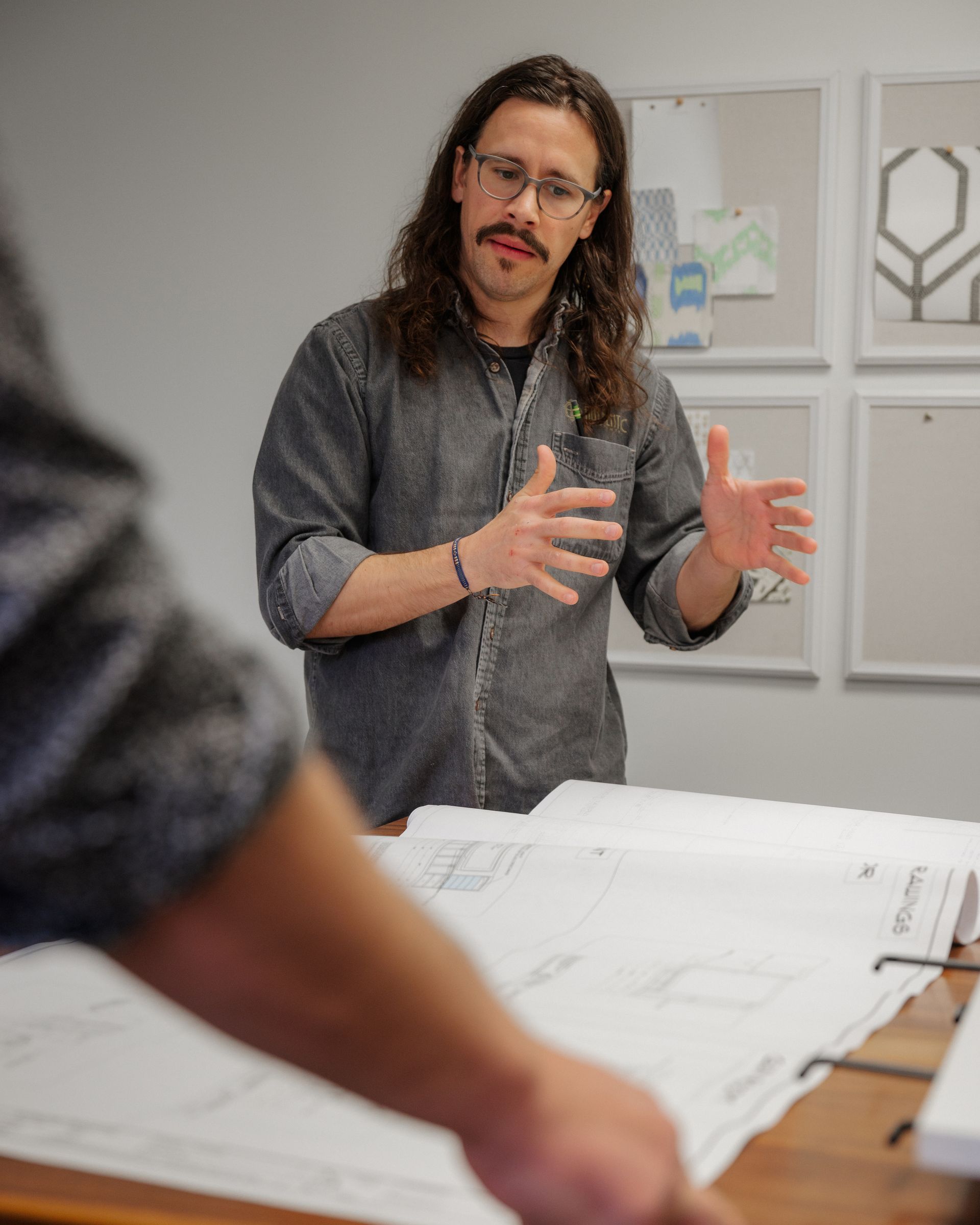 Man gesturing over design sketches in a bright office with framed artwork on the wall