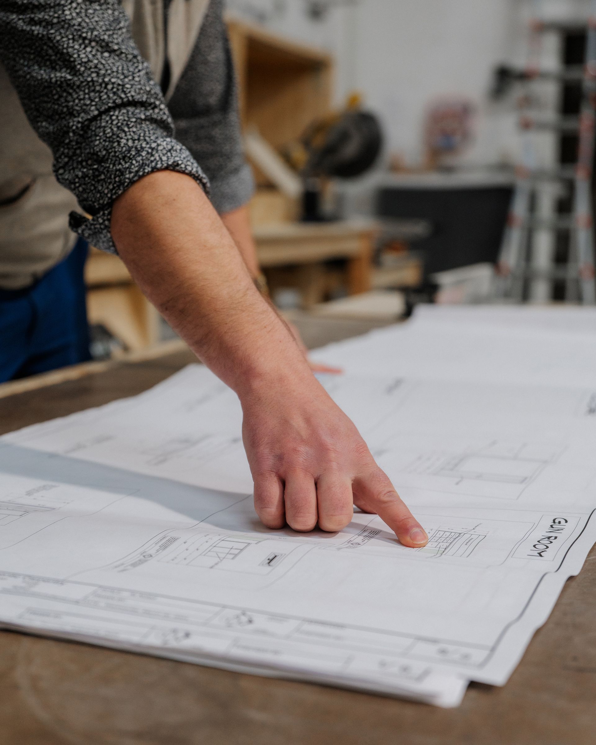 Person pointing at architectural blueprints on a table in a workshop
