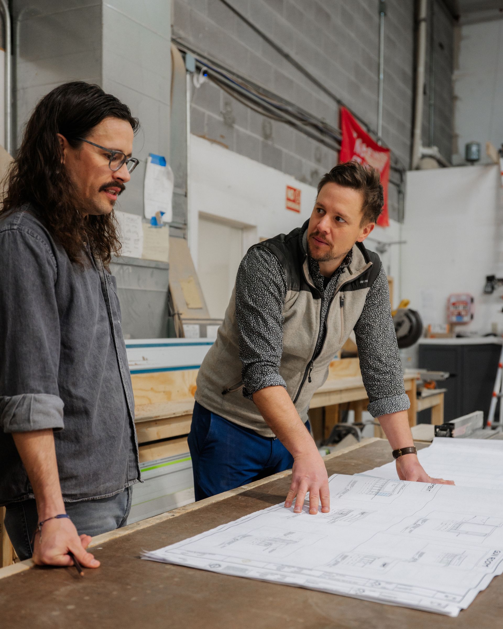 Two people reviewing blueprints on a workbench in a workshop