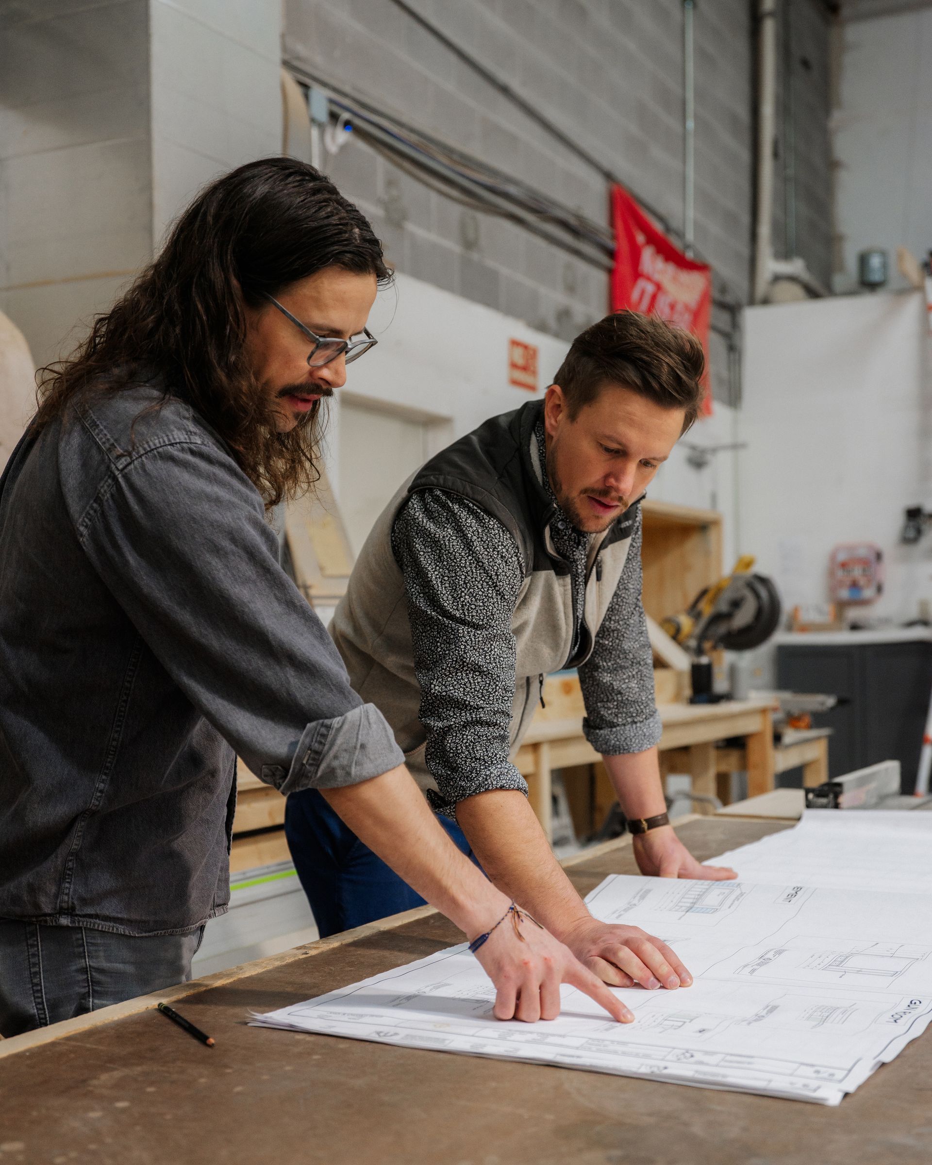 Two people leaning over a large blueprint on a worktable in an industrial workshop