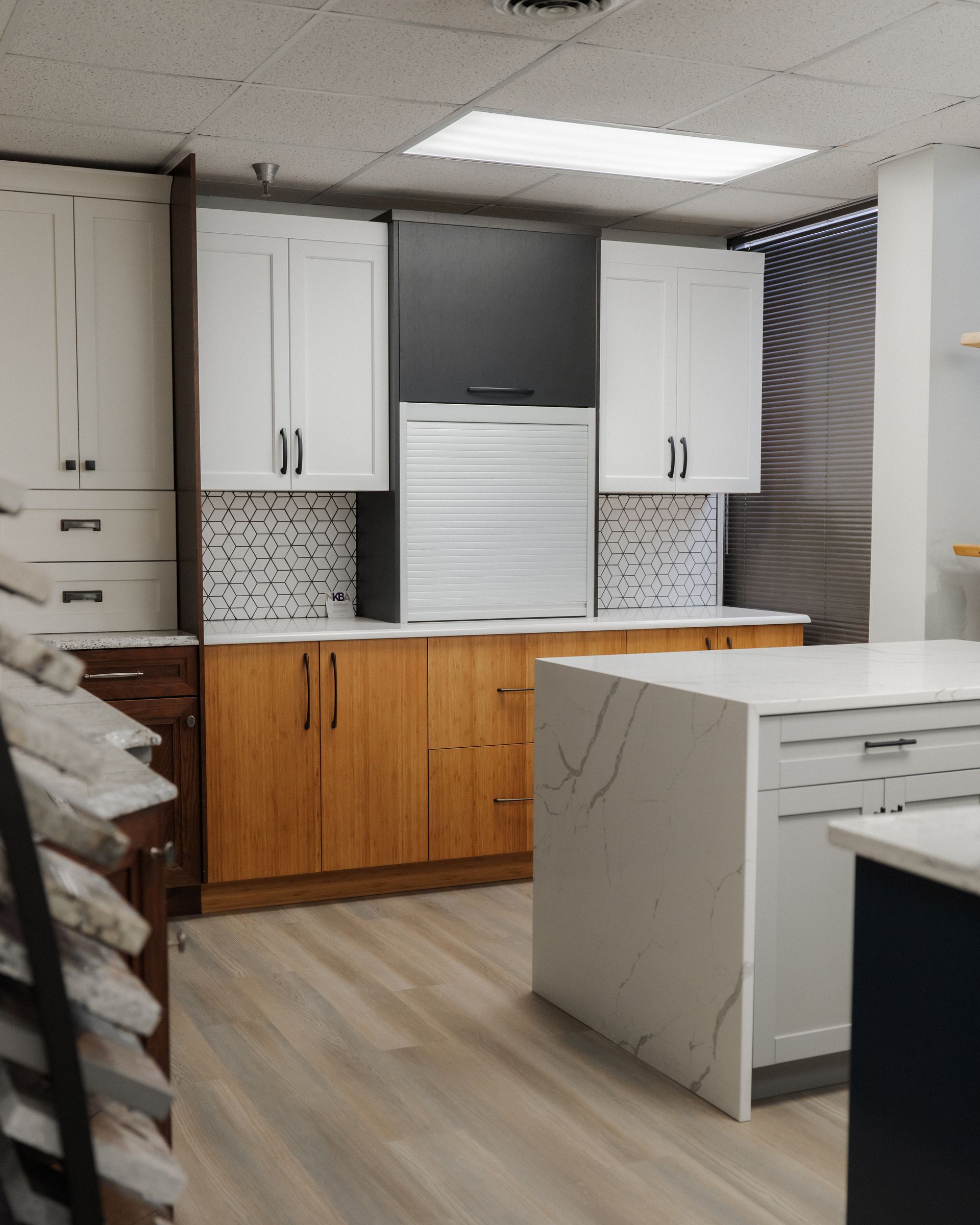 Empty kitchen showroom with white cabinets, wood lower cabinets, and a white island countertop