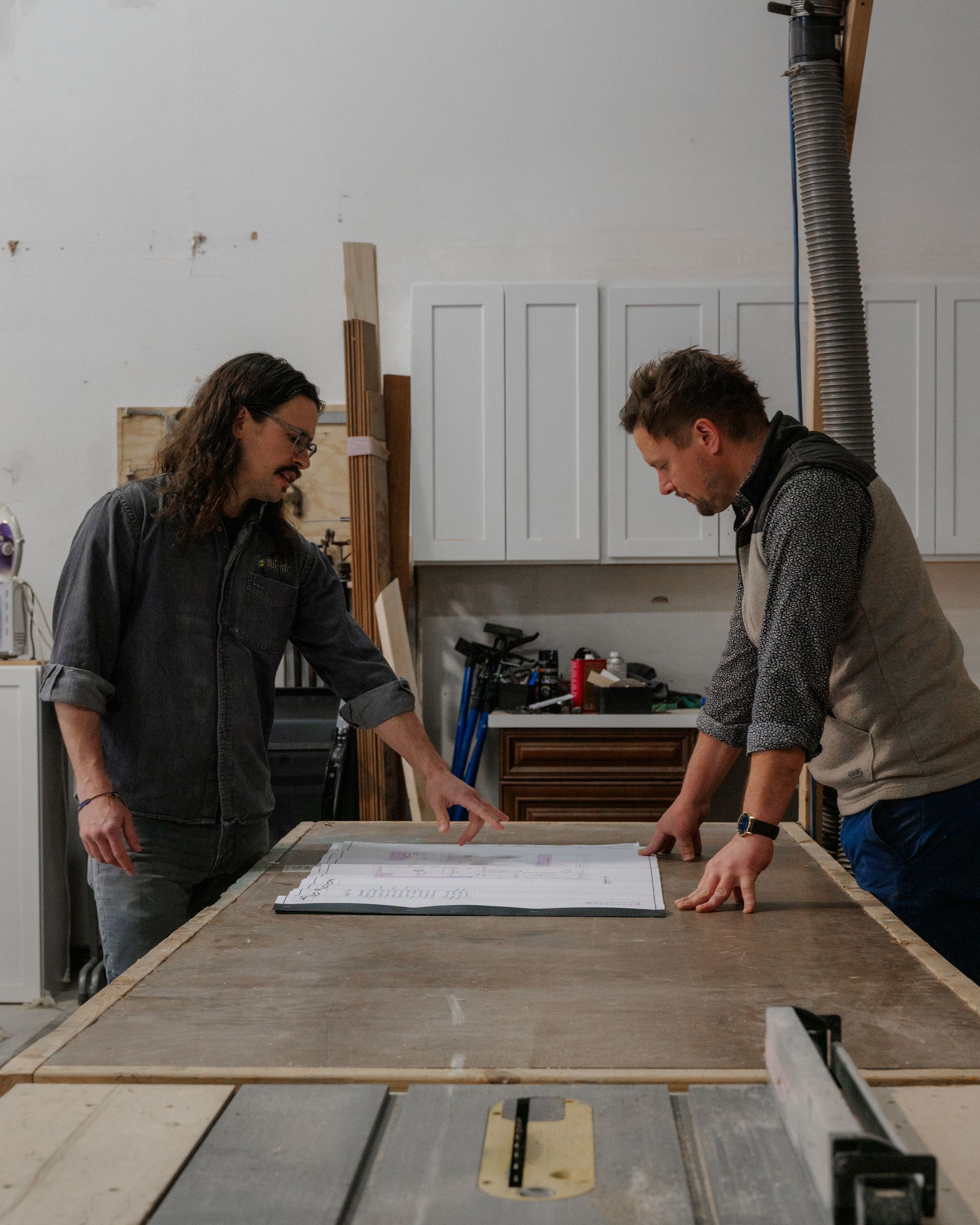 Two people measuring a plywood sheet on a workbench in a workshop