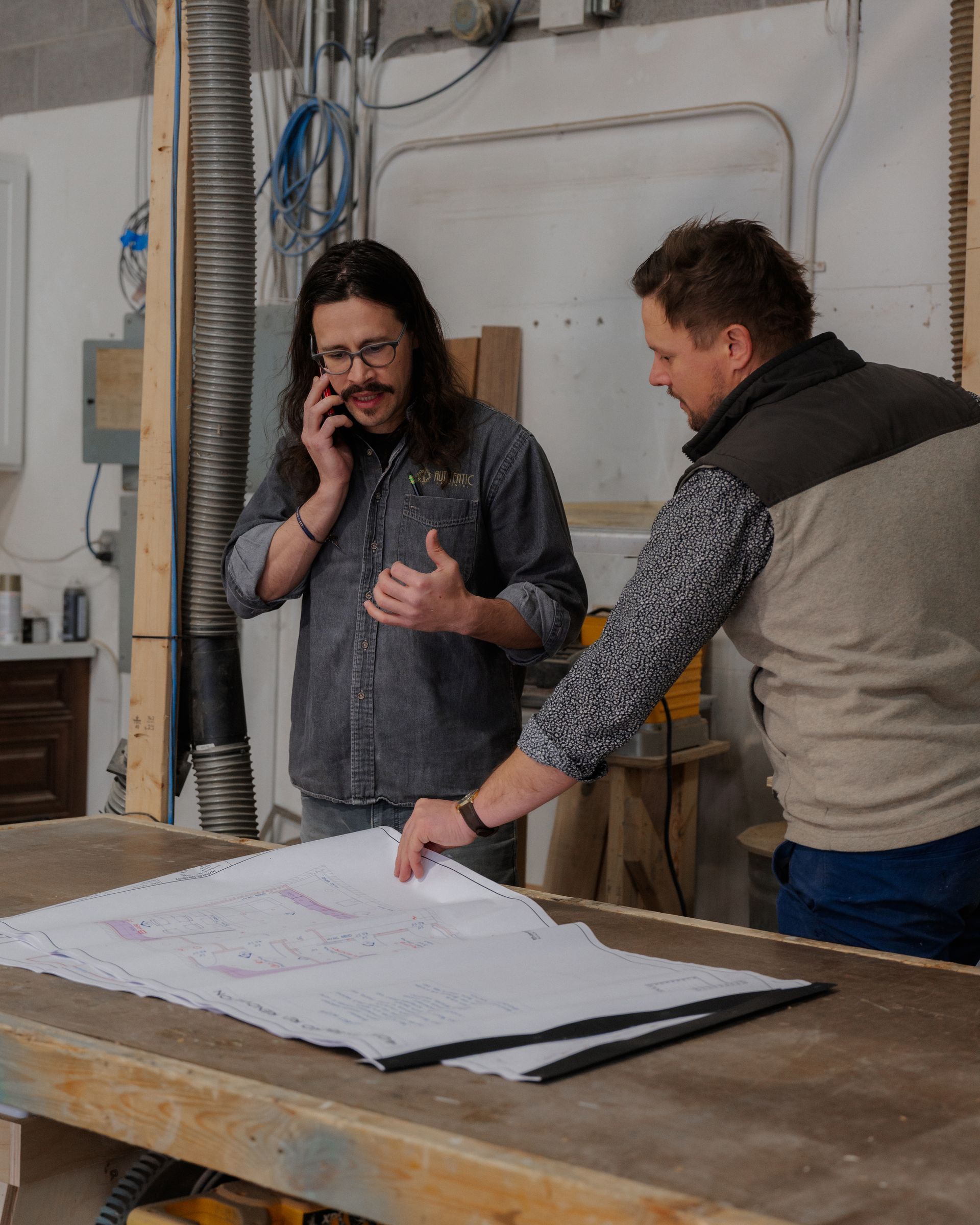 Two men reviewing large blueprints on a worktable in a workshop