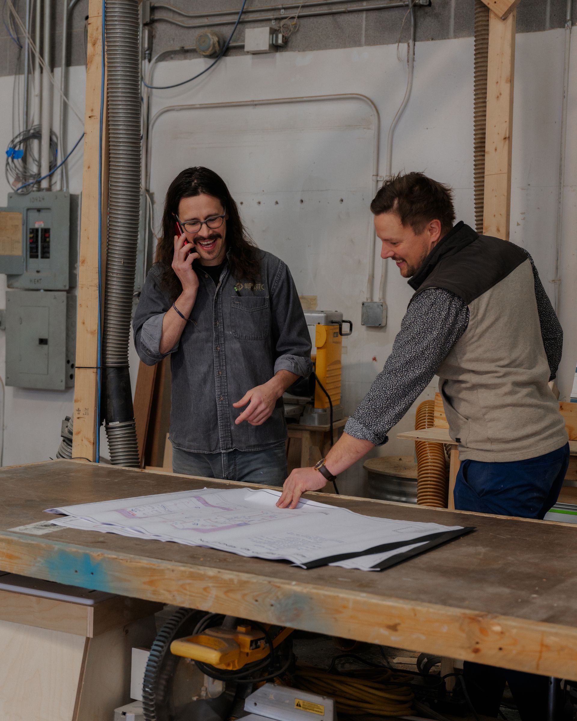 Two people in a workshop review a large sheet of paper on a worktable.