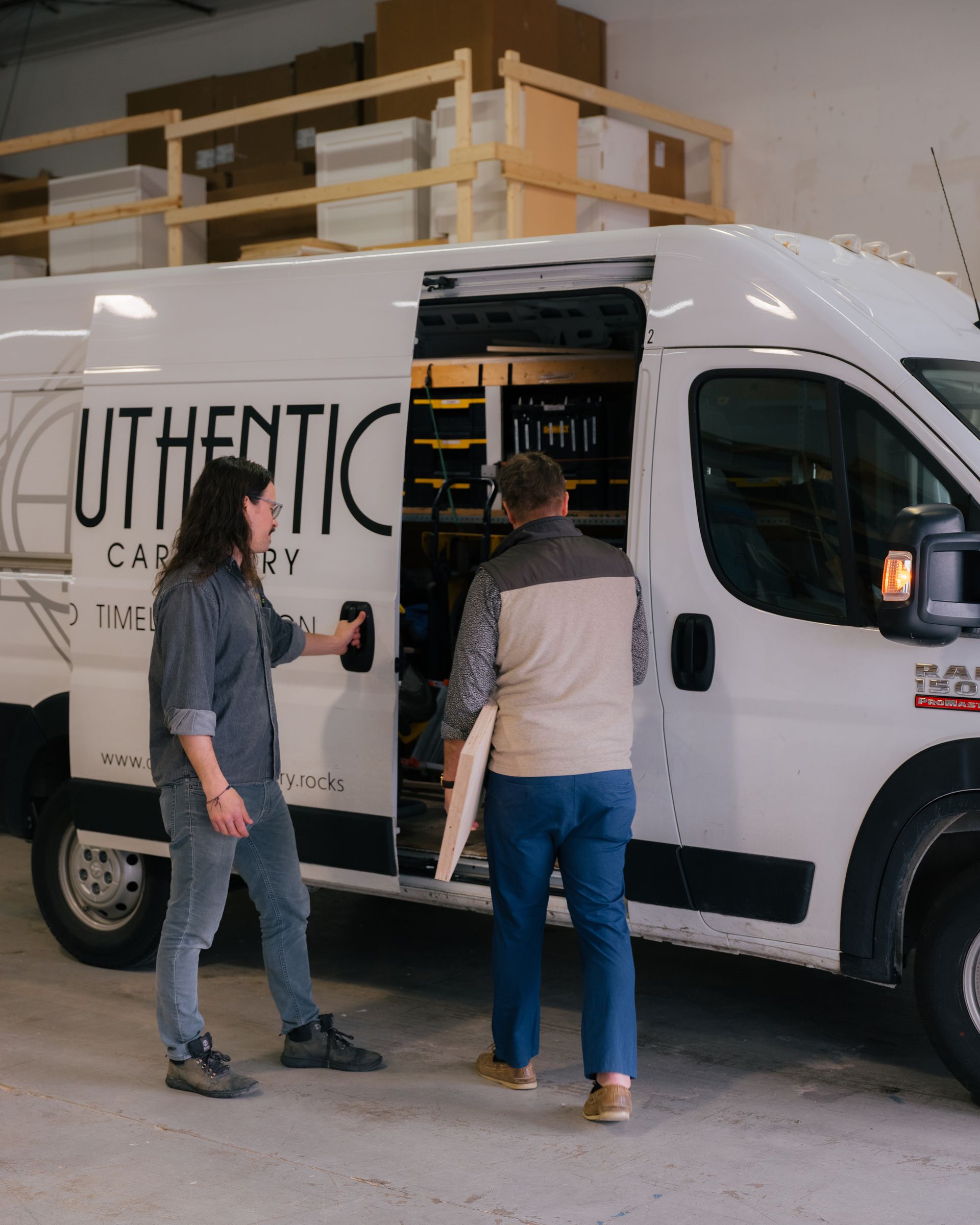 Two people stand by a white van with open side door at an indoor event booth.