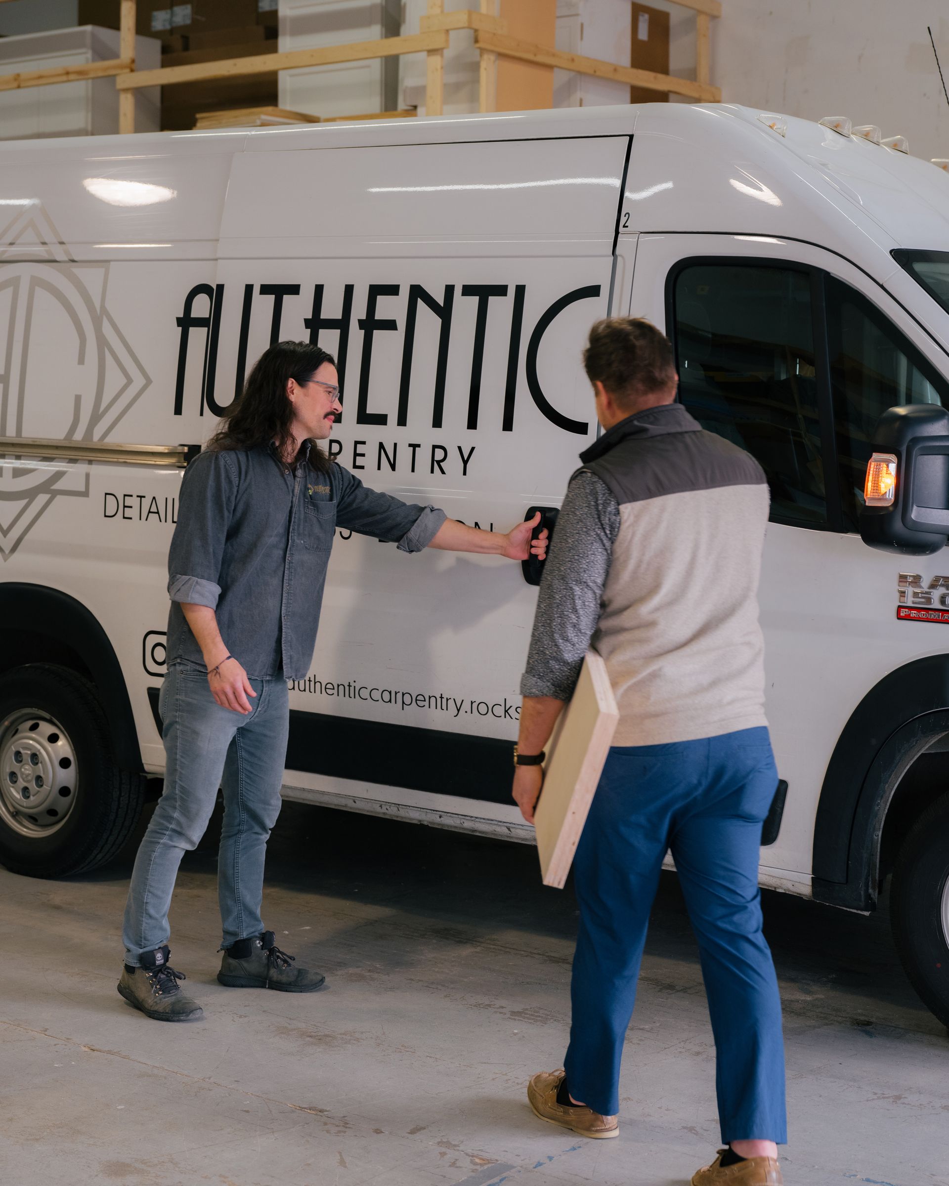 Two people exchanging a package beside a white authentication van.