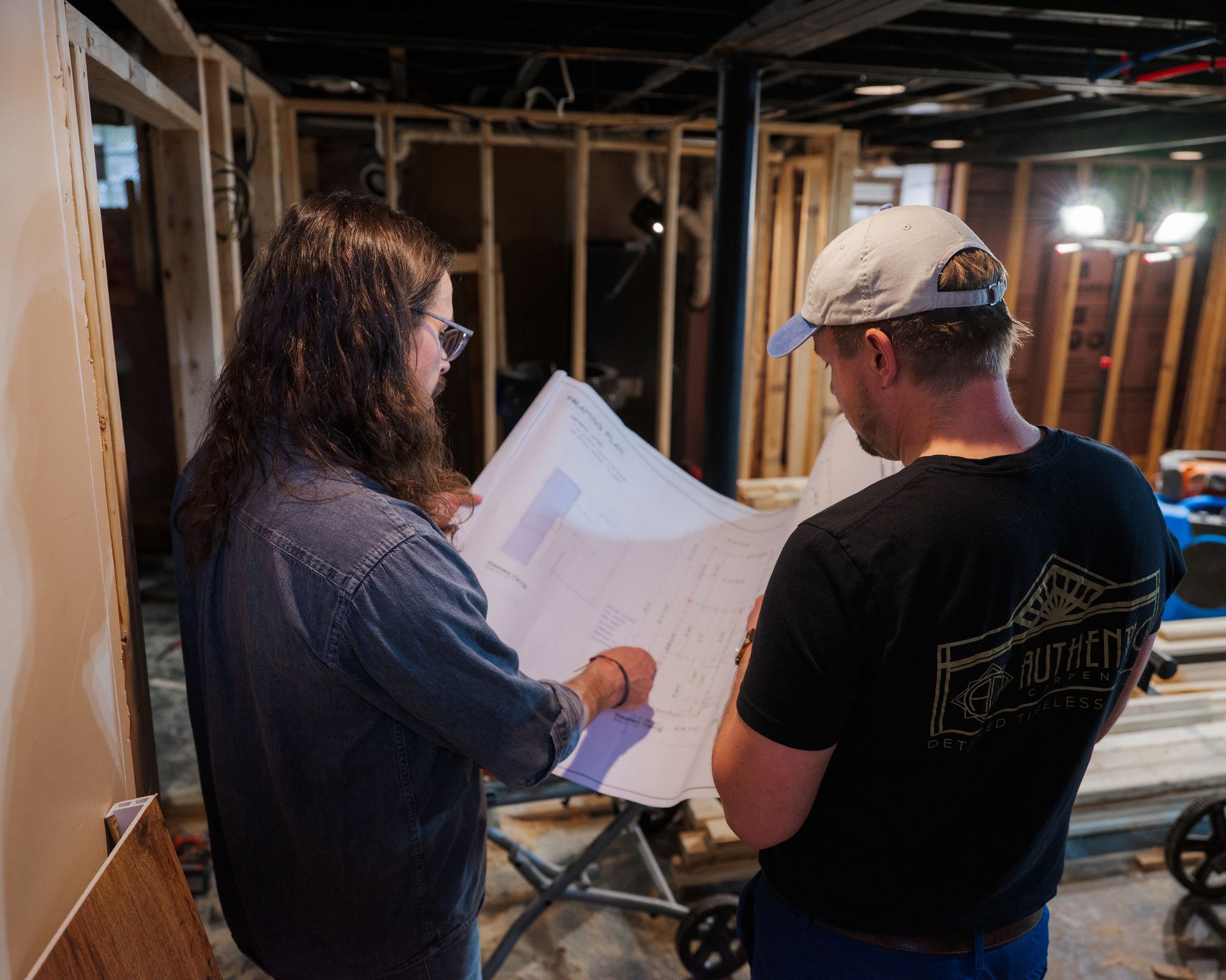 Two people reviewing строительные plans in a basement under construction