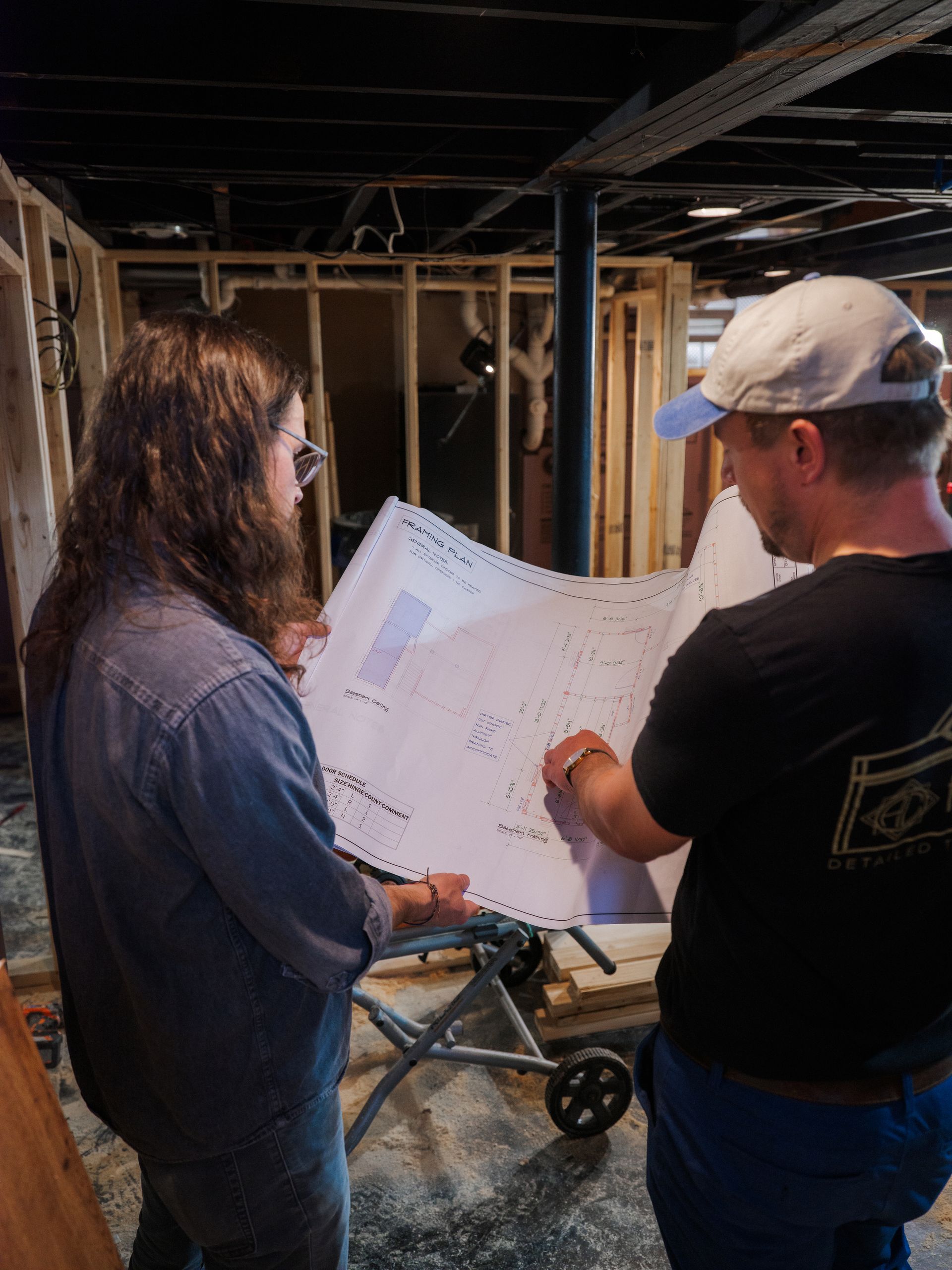 Two people reviewing a large blueprint in a bare construction site basement.