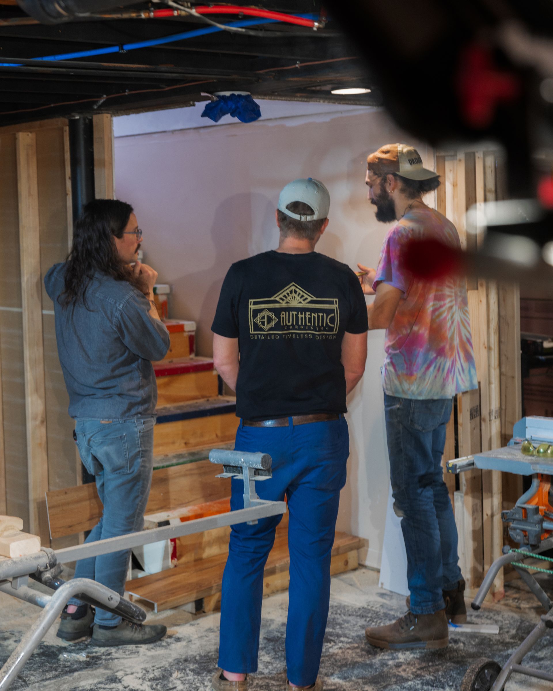 Three people talk inside an unfinished room with exposed beams and construction scaffolding.