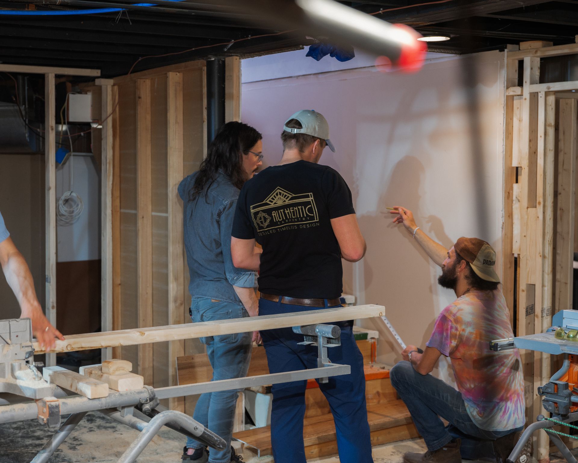 People working inside an unfinished room, with one kneeling and pointing at a wall under construction.