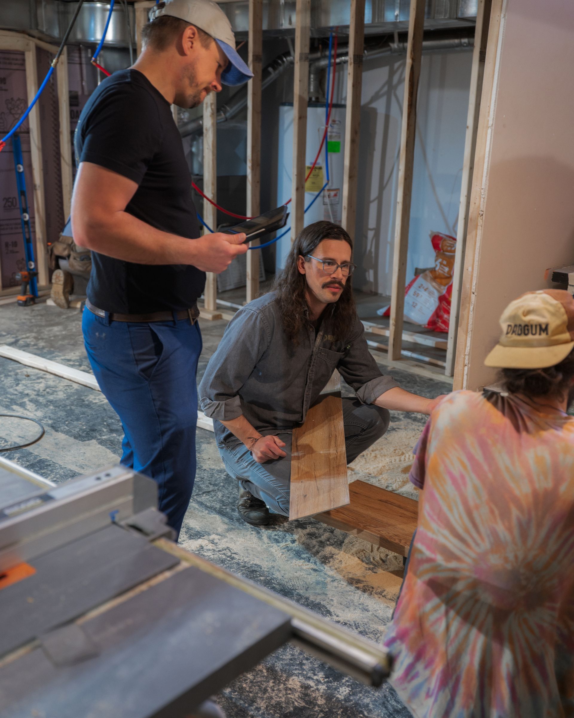 Three people discussing floor plans at a construction site with exposed framing and tools nearby