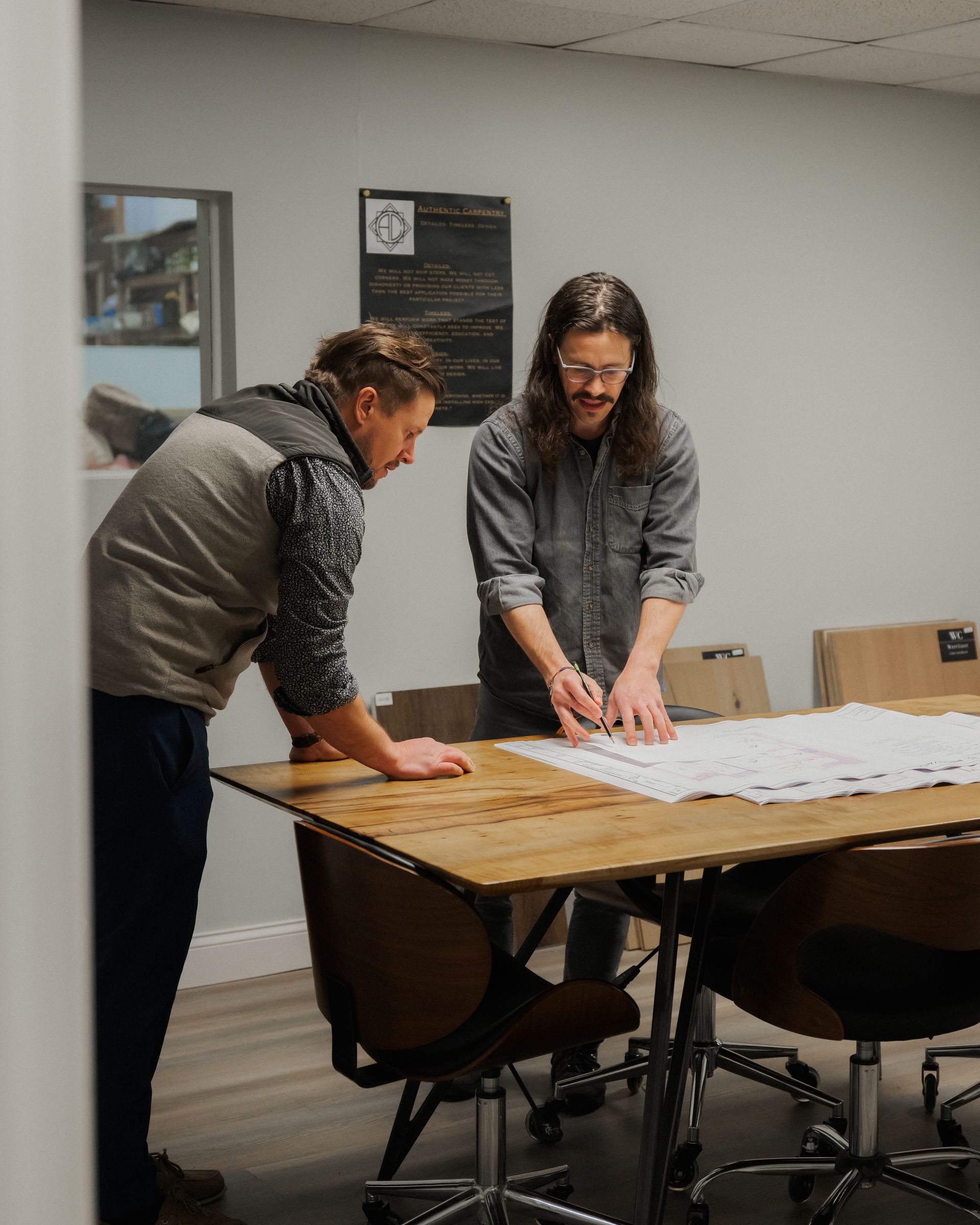Two people leaning over a conference table, reviewing large papers in a meeting room.
