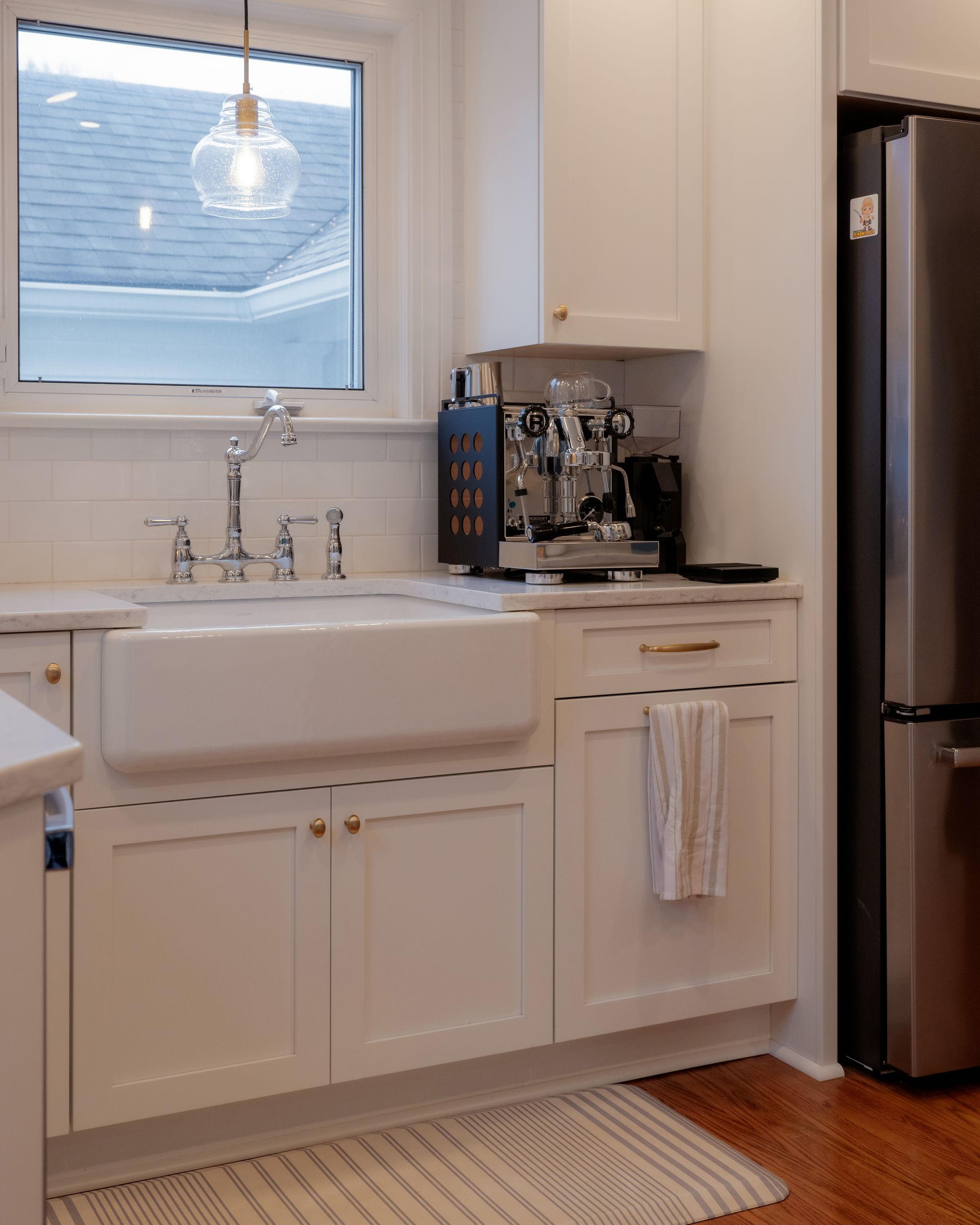 Bright white kitchen sink under a window with coffee maker and stainless fridge