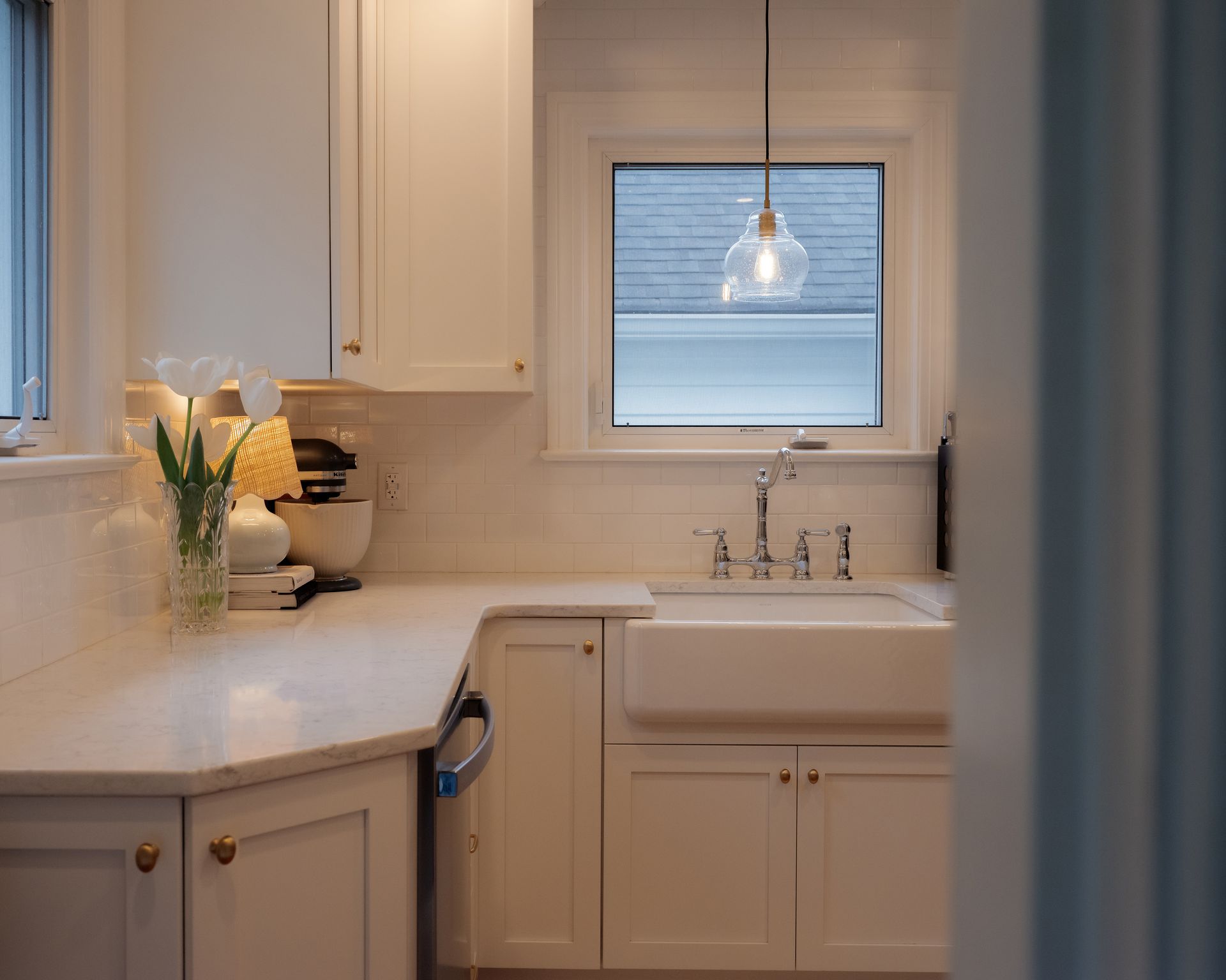 Bright kitchen with white cabinets, farmhouse sink, and a vase of flowers by the window.