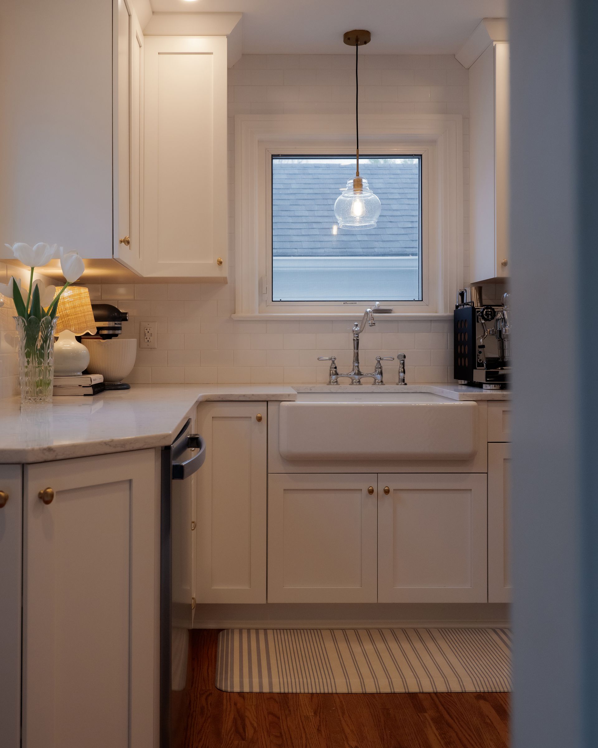Bright white kitchen with a sink under a window and a woven rug on the floor.