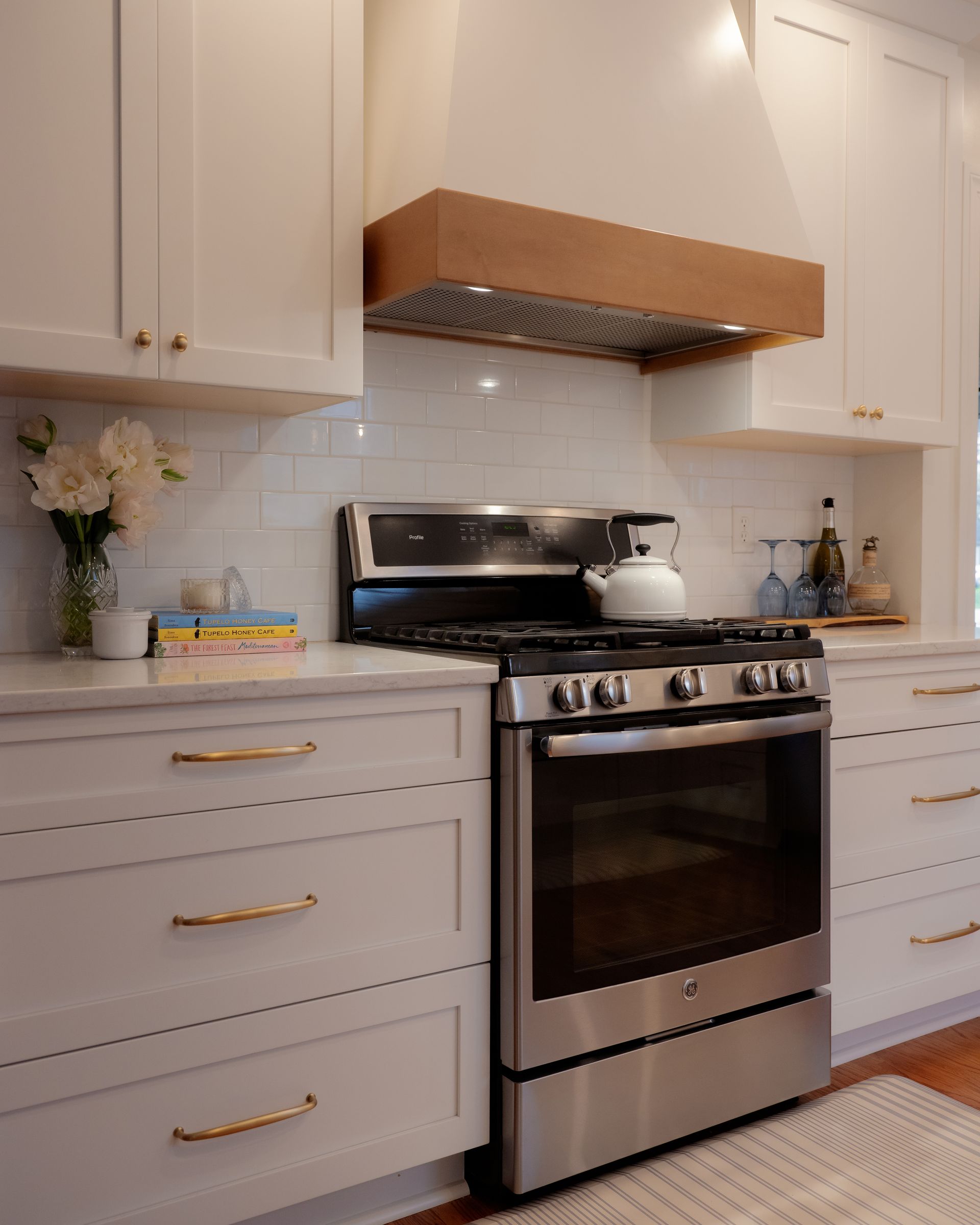 Modern kitchen with white cabinets, stainless steel stove, and a wood range hood under bright lighting