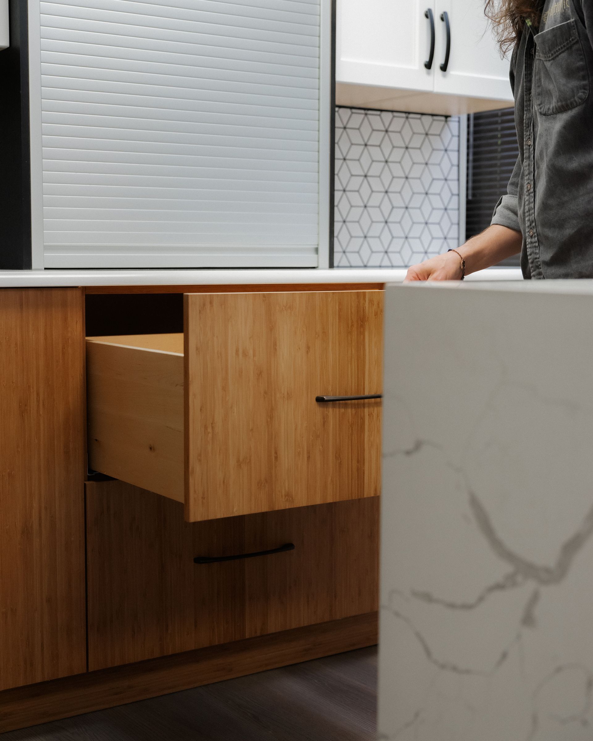 Modern kitchen with a wood drawer open beside a white marble island and tiled backsplash.