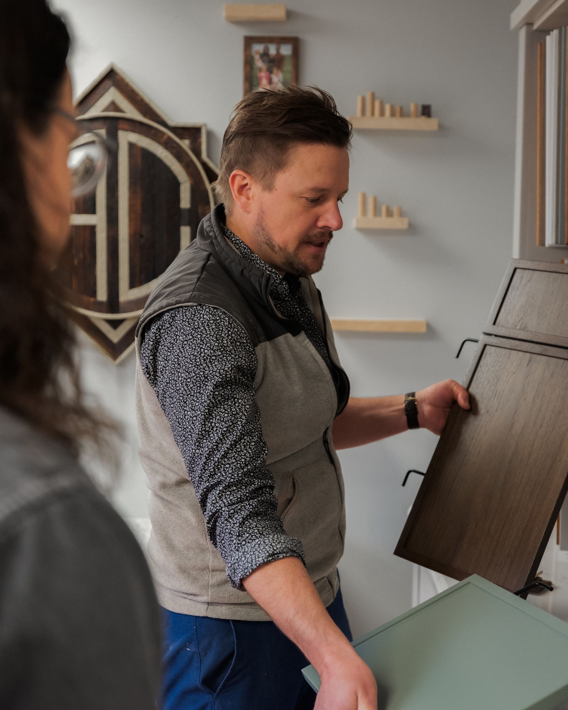 Man in a gray apron handles large dark wood panel in a bright workshop