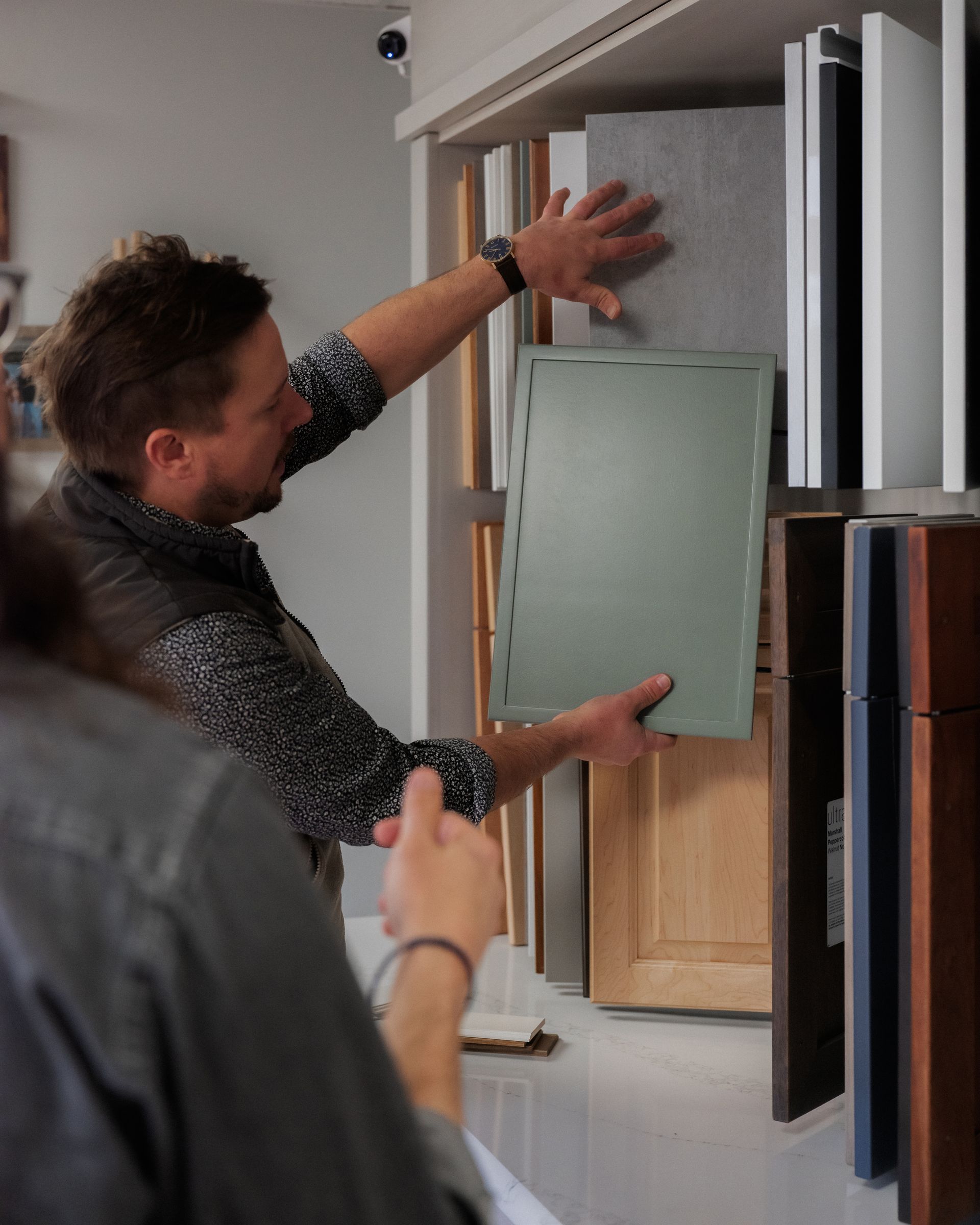Person holding up a green glass cabinet panel in a showroom, inspecting shelving samples.