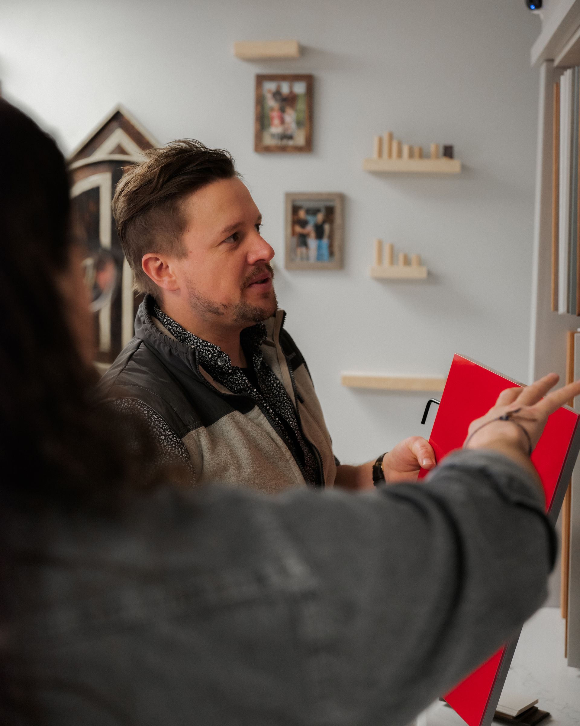 Two people discussing a red notebook beside a wall-mounted screen in a bright room