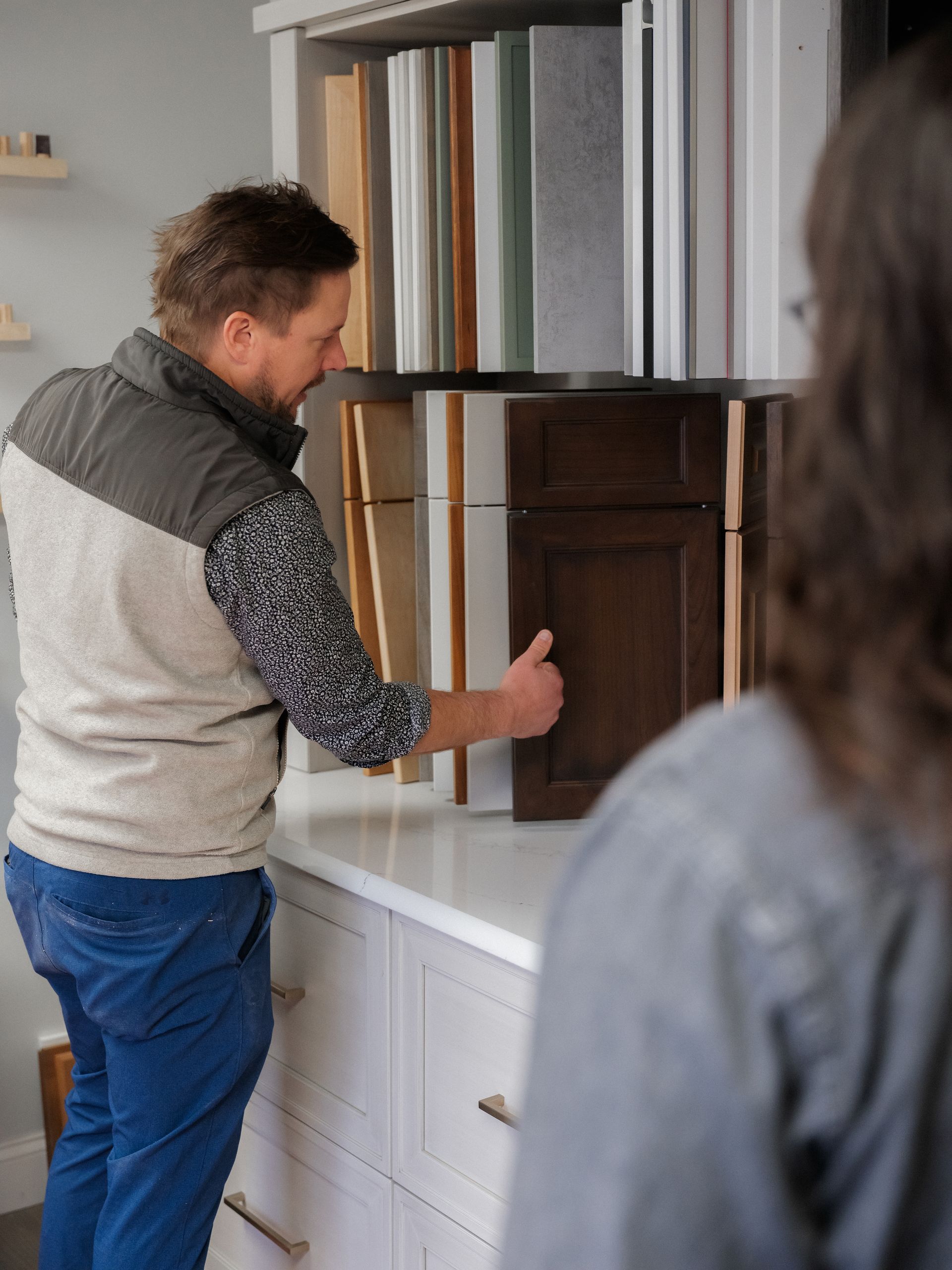Person reaching into a cabinet while another stands nearby in a room with shelves and drawers