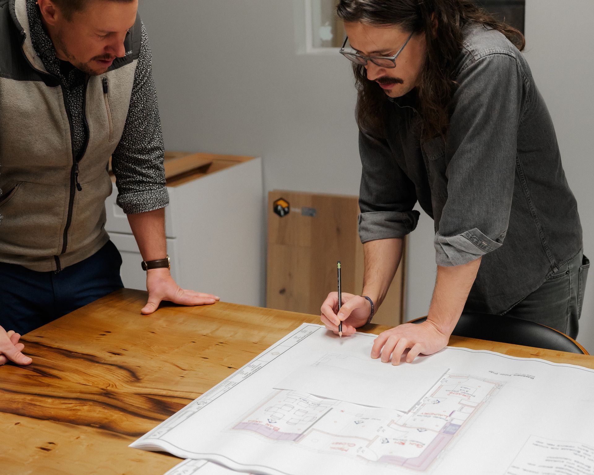 Two people lean over a table reviewing a large architectural plan while one points with a pen.