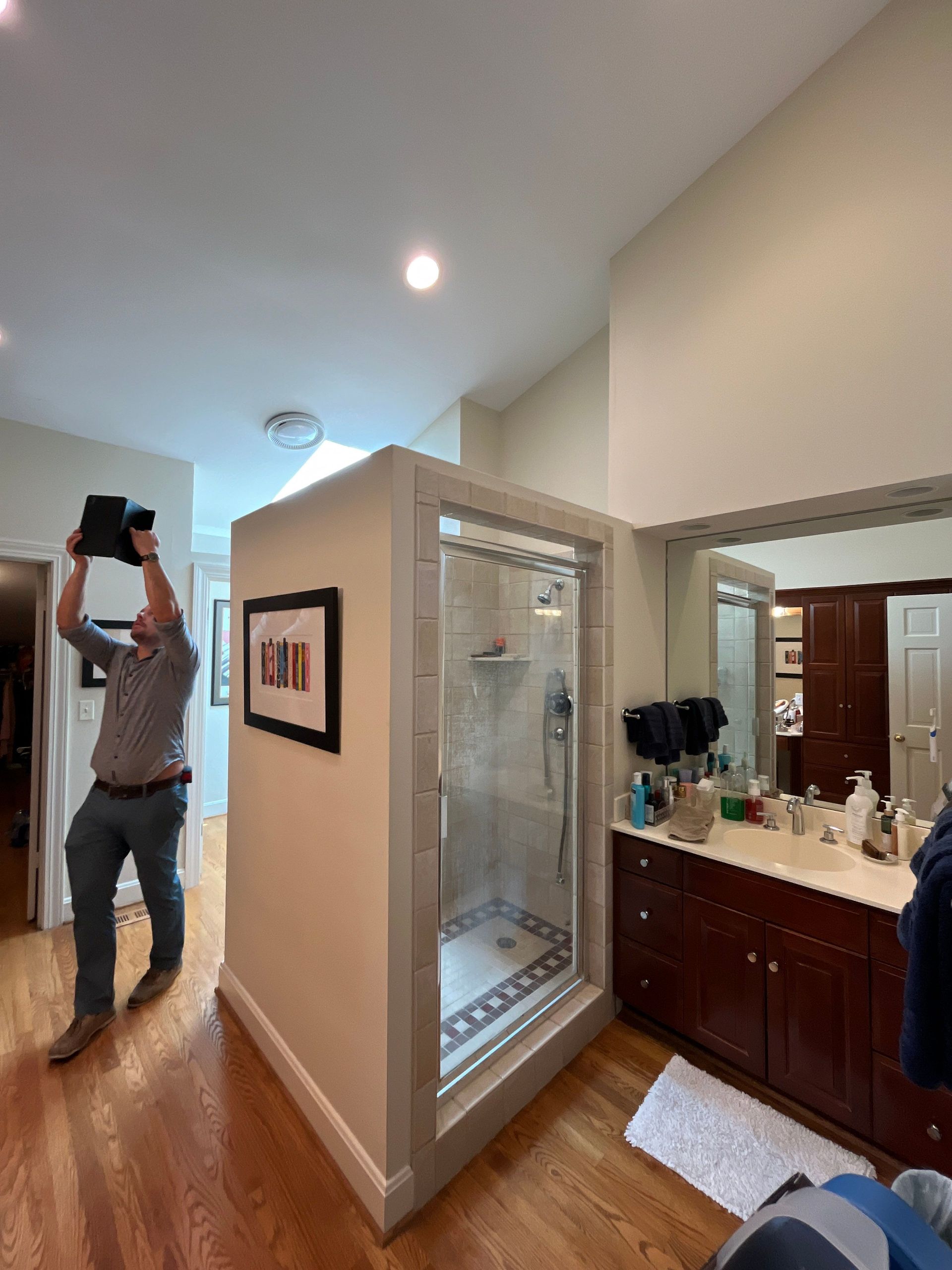 Hallway with a glass shower enclosure, vanity, and a person standing near a doorway.