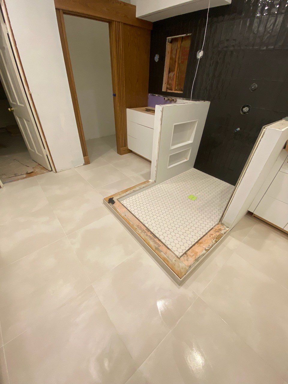 Bathroom under renovation with tiled floor, open doorway, vanity, and a shower curb in the foreground