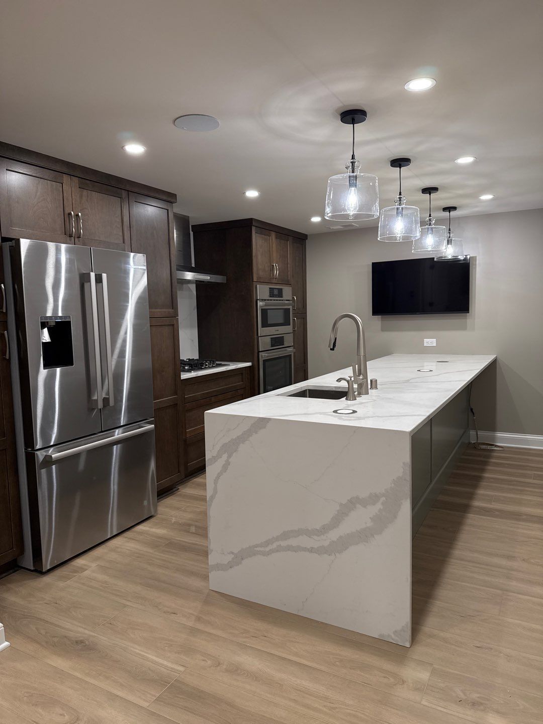 Modern kitchen with stainless steel appliances, wood cabinets, and a large white marble island with pendant lights.