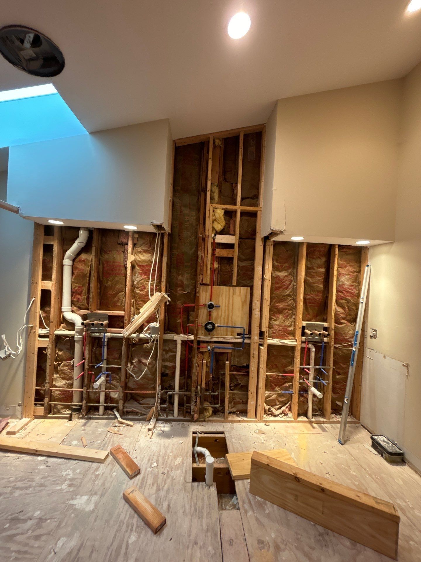 Kitchen wall under renovation with exposed studs, plumbing, and debris on the floor